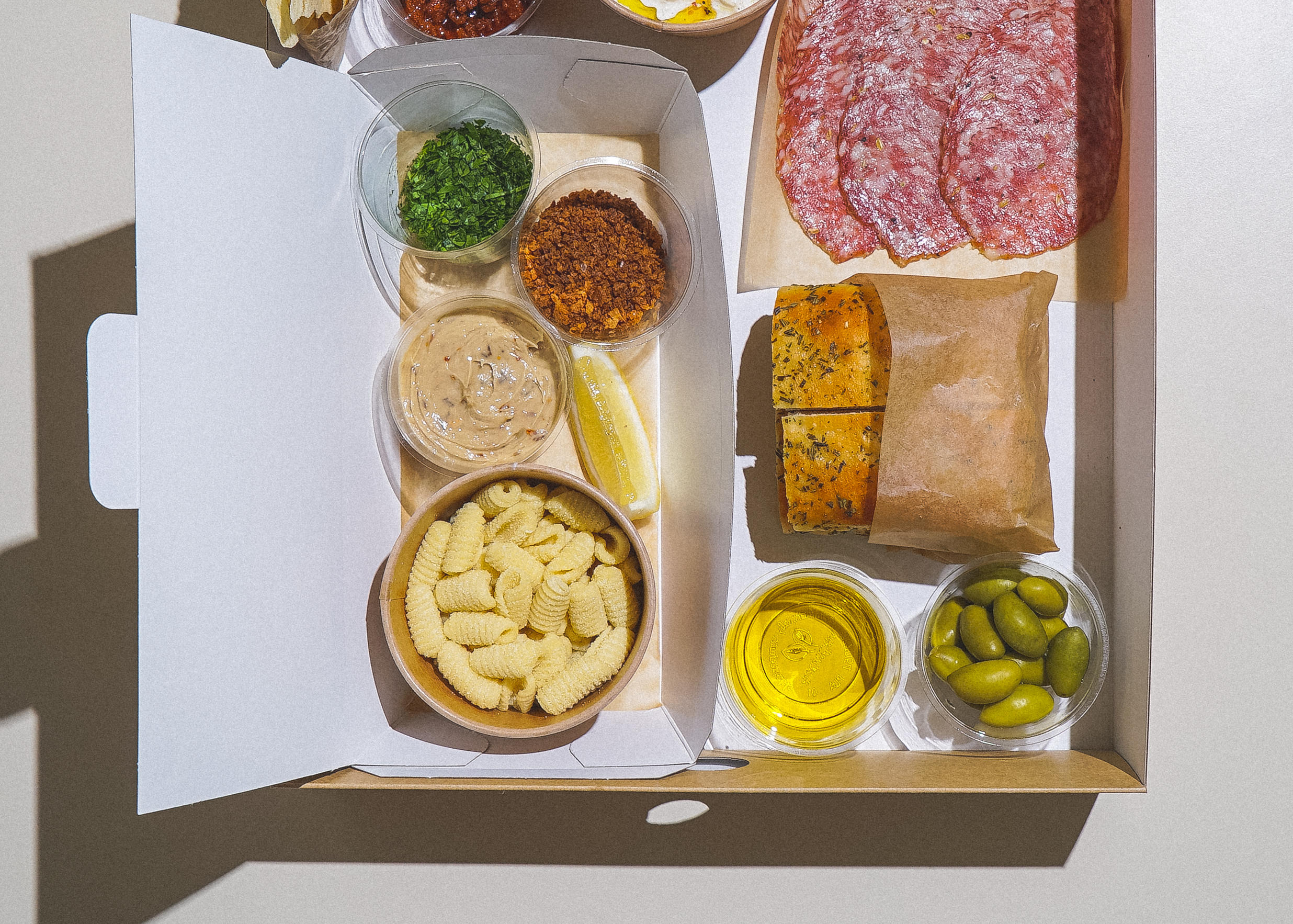 Fresh pasta, sauce, salumi, foccaccia, and olives in a cardboard meal kit box, shot from a birdseye view
