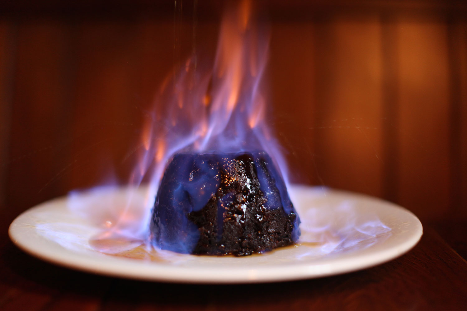 An enthusiastically flambéd Christmas pudding, licked by blue and orange flame