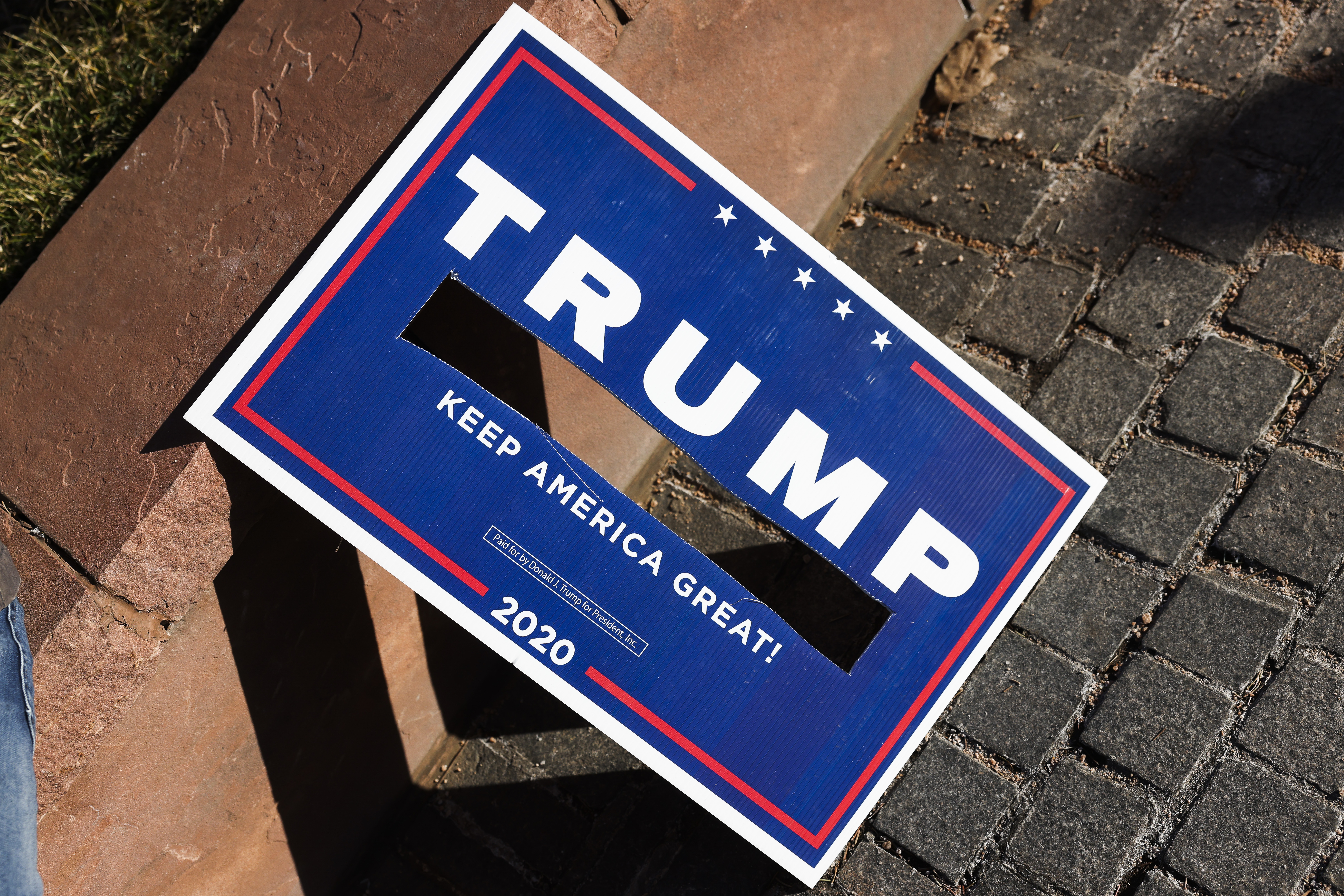 A Trump campaign sign with a hole in it where Pence’s name was, on a walkway leaning against a curb.