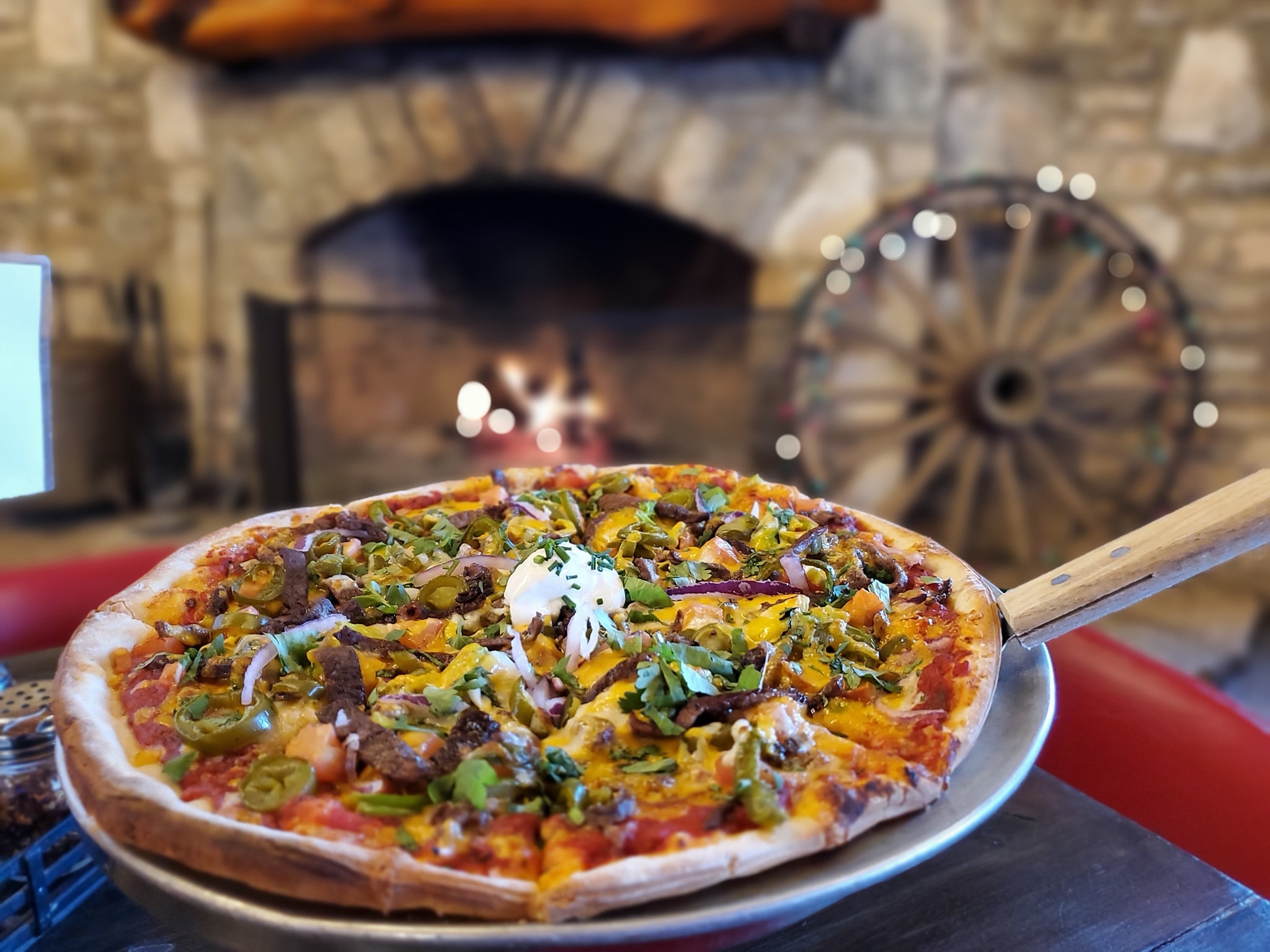 Pizza on a metal pan in front of a stone fireplace