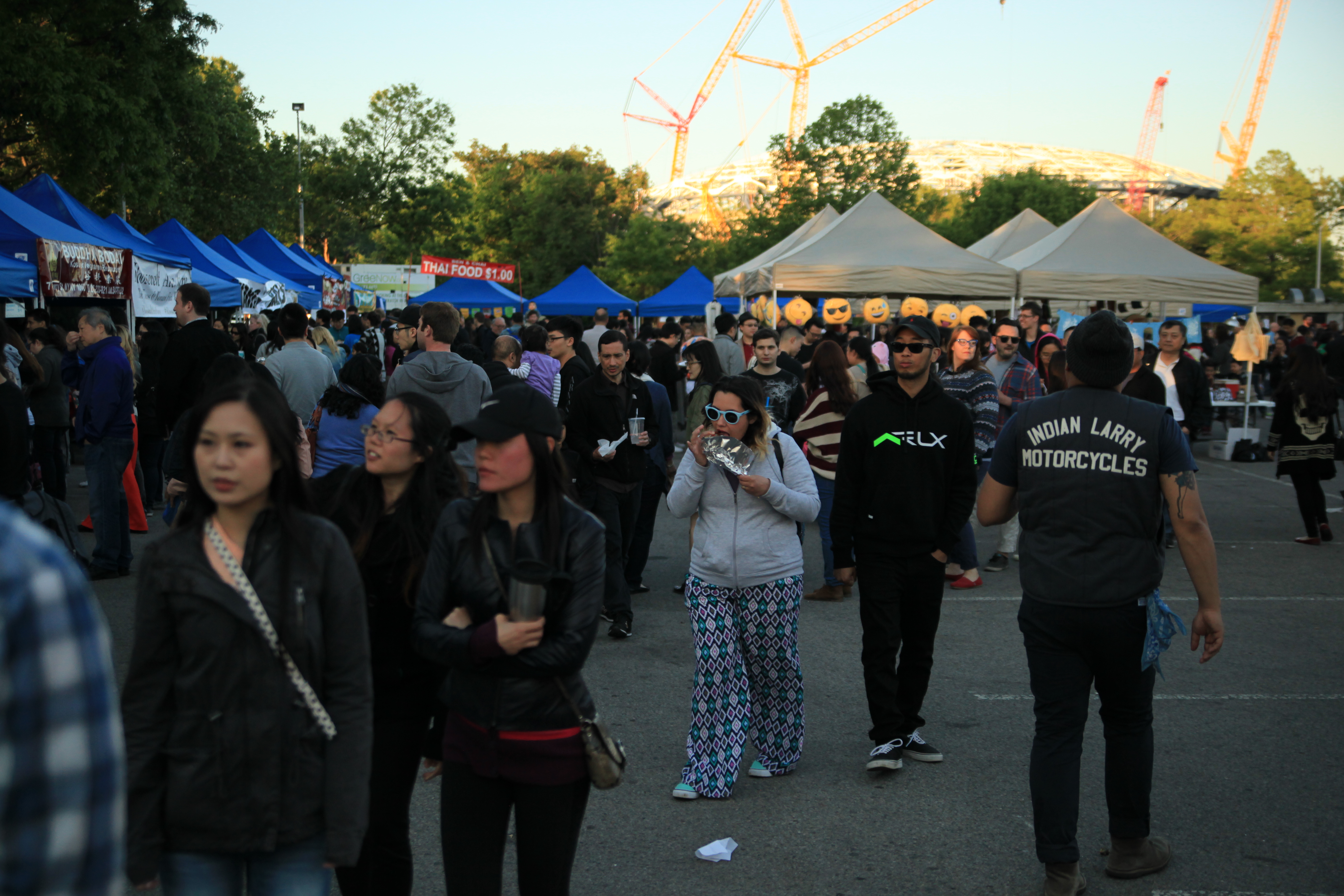 A group of people walking around the Queens Night Market at dusk.