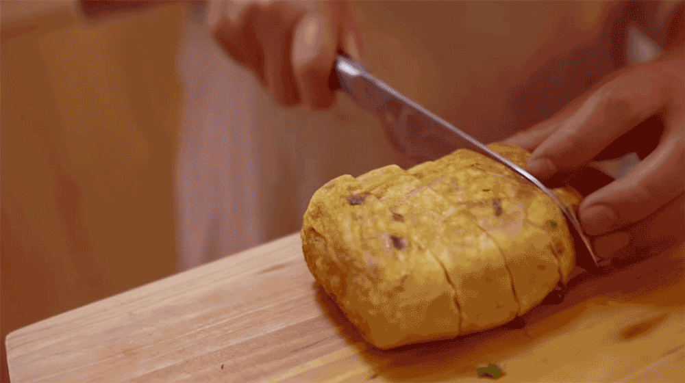 Moving .gif of two hands cutting into and separating pieces of a rolled-up egg omelet.