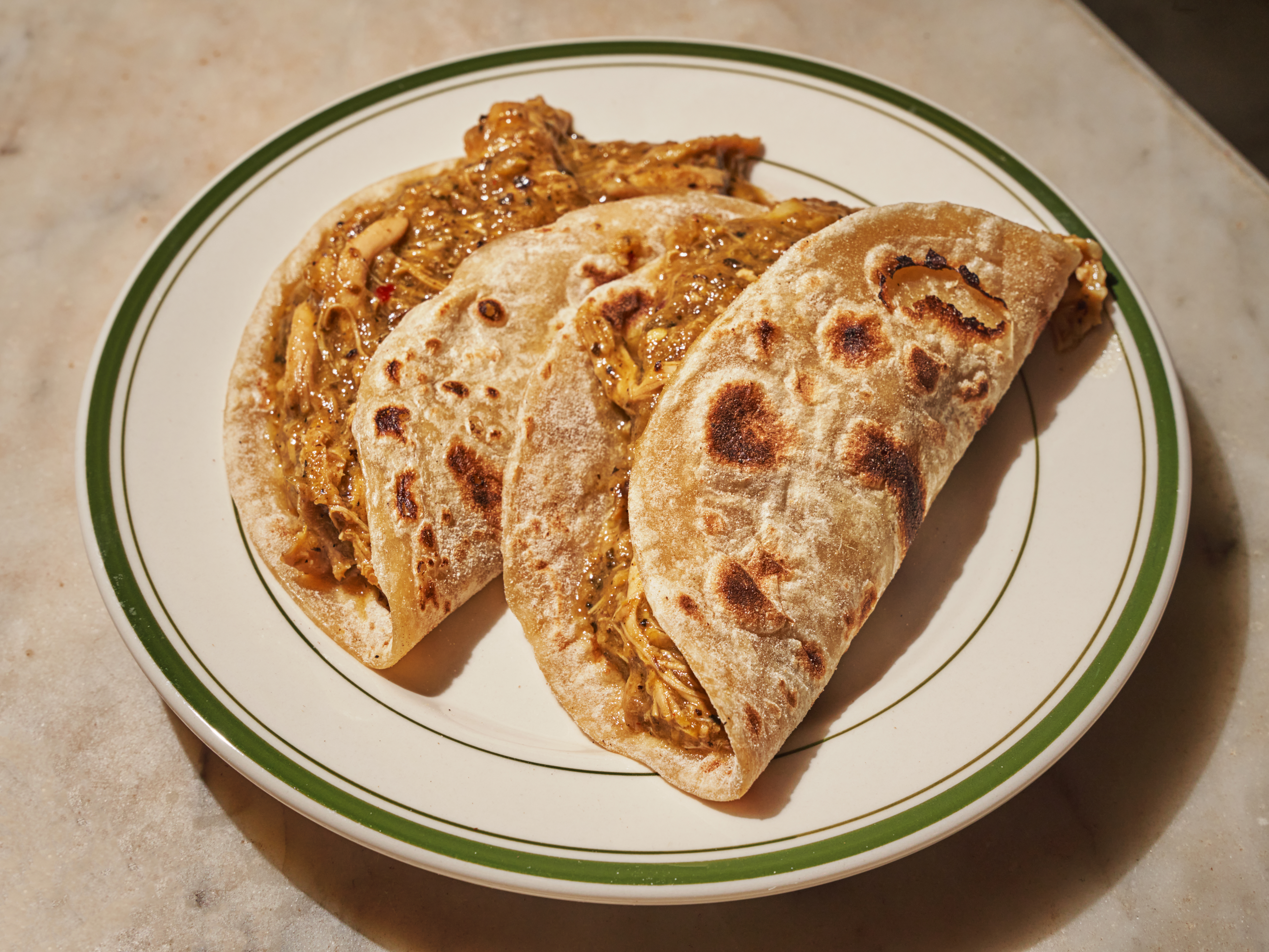 Two lightly charred flour tortillas are stuffed with pollo guisado on a plate