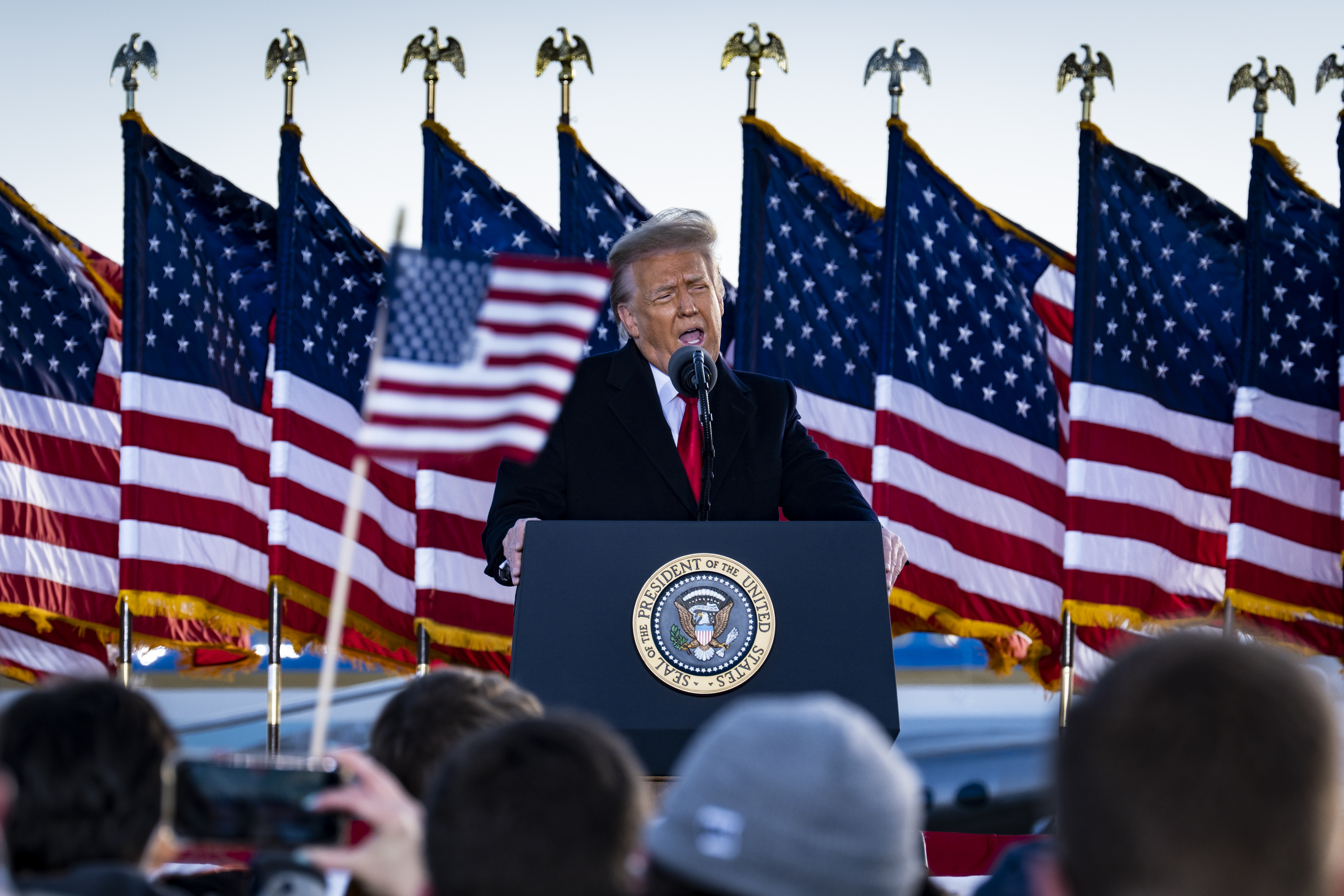 President Trump backed by American flags and speaking to a small crowd on the tarmac at Joint Base Andrews.