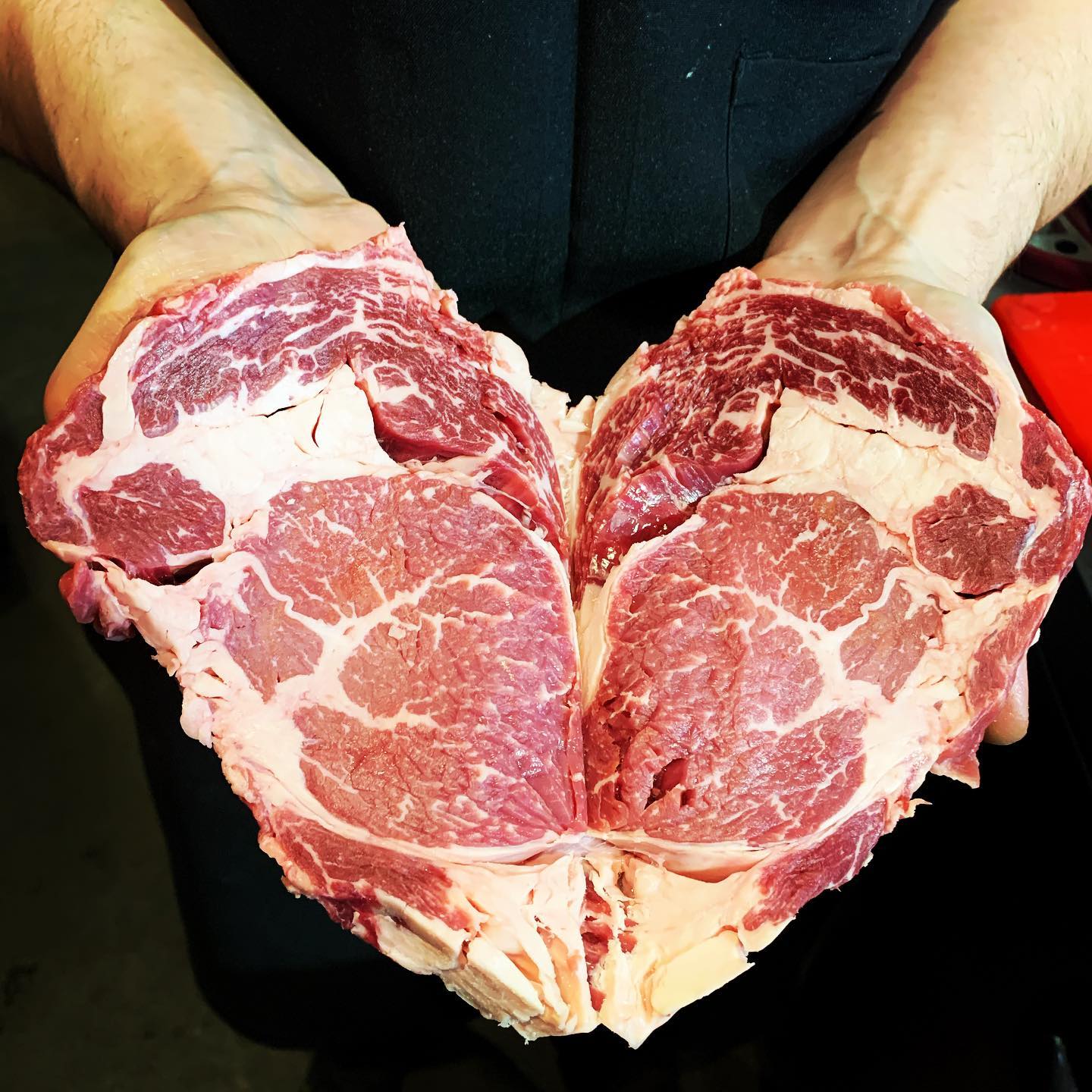 a person holding two raw cuts of steak in the shape of a heart