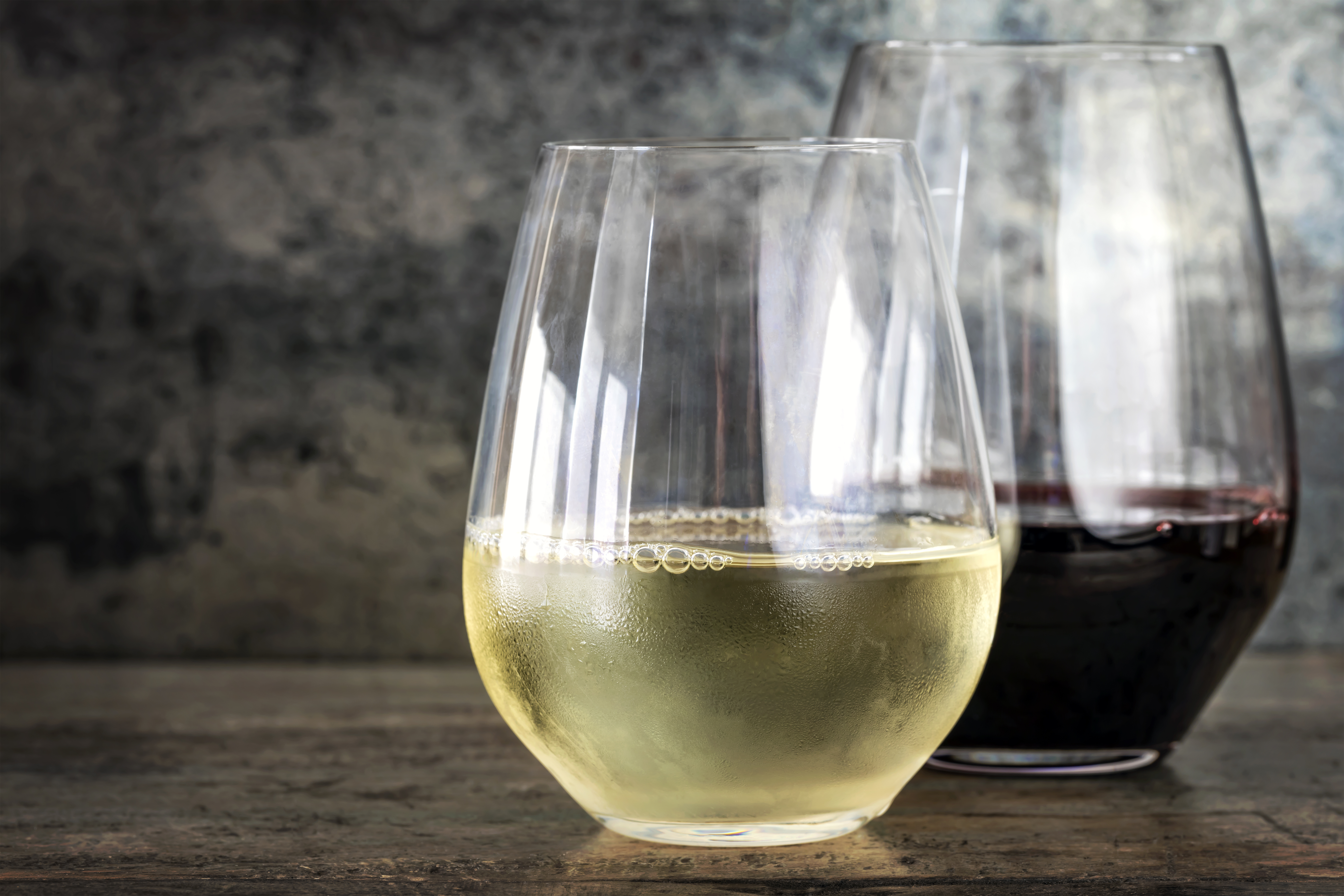 A stemless wine glass filled with white wine in front of a stemless glass filled with red wine