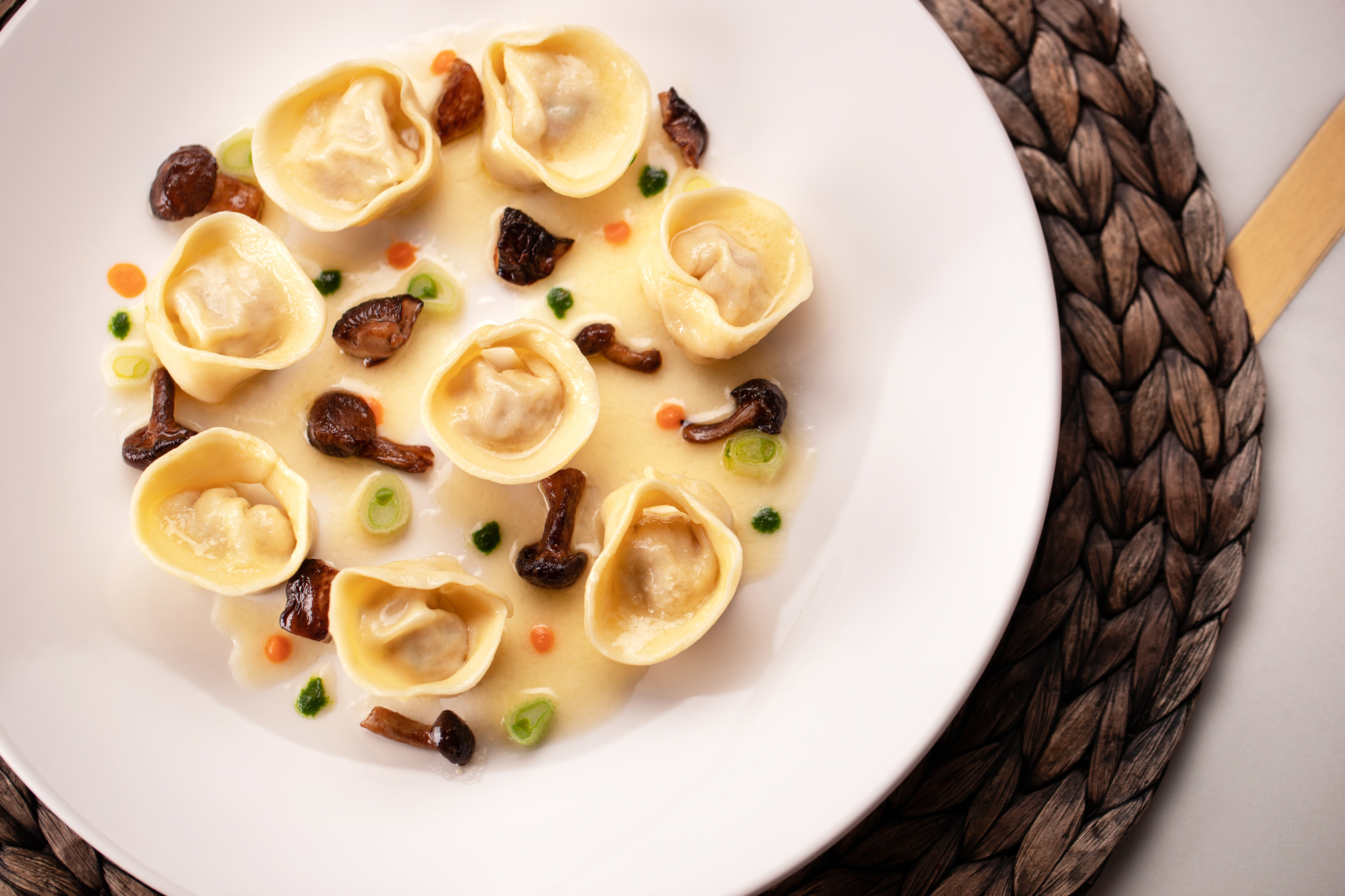 A white plate with tortelli in a white sauce with mushrooms