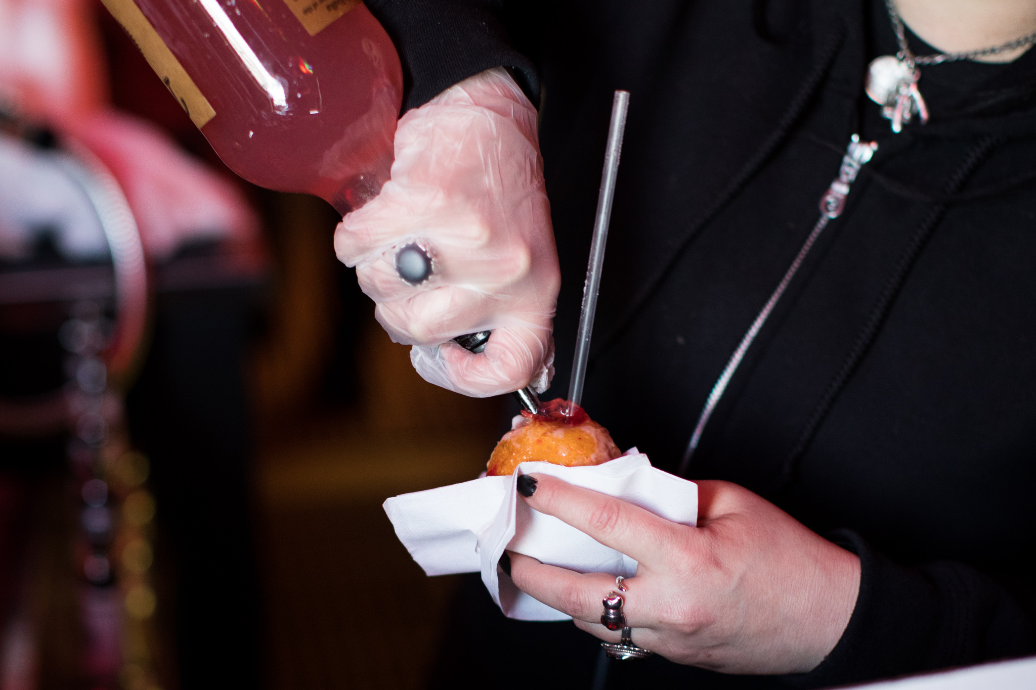 A bartender pours liquor into a raspberry paczki with a straw.