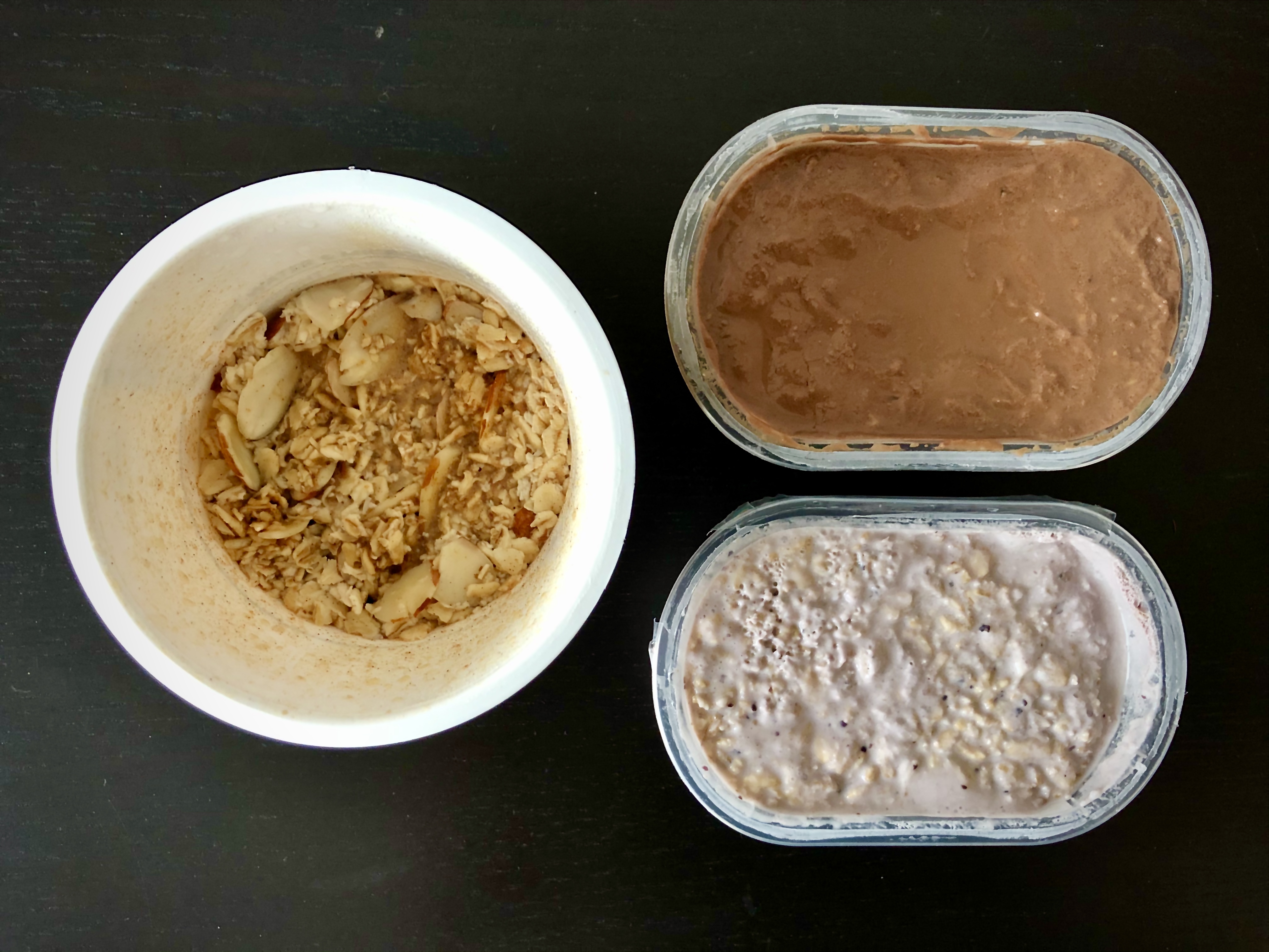 A circular container of overnight oats sits next to two rectangular containers of overnight oats, one purple and one brown.