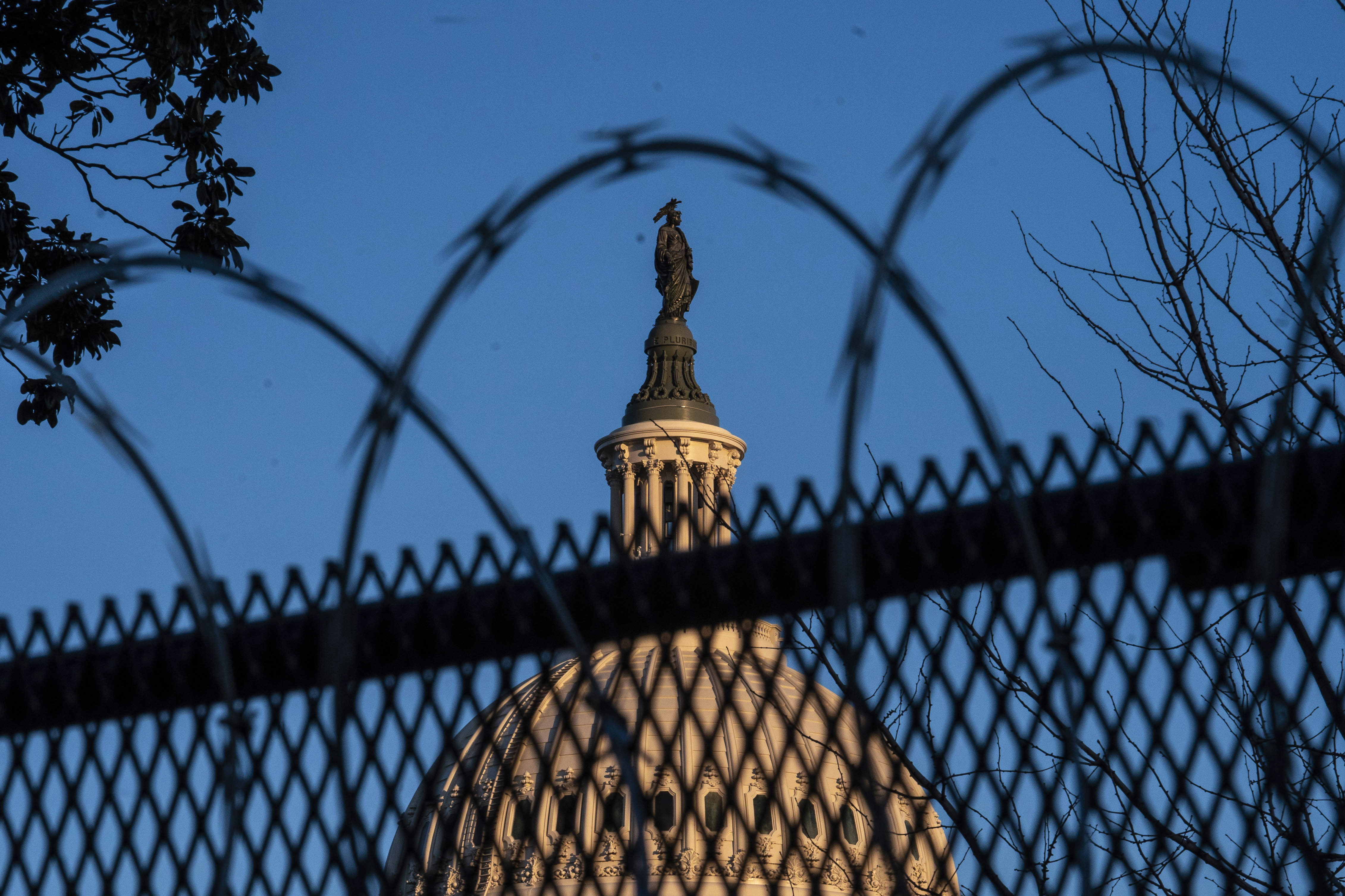 The top of the US Capitol building seen through a razor-wire-topped fence. 