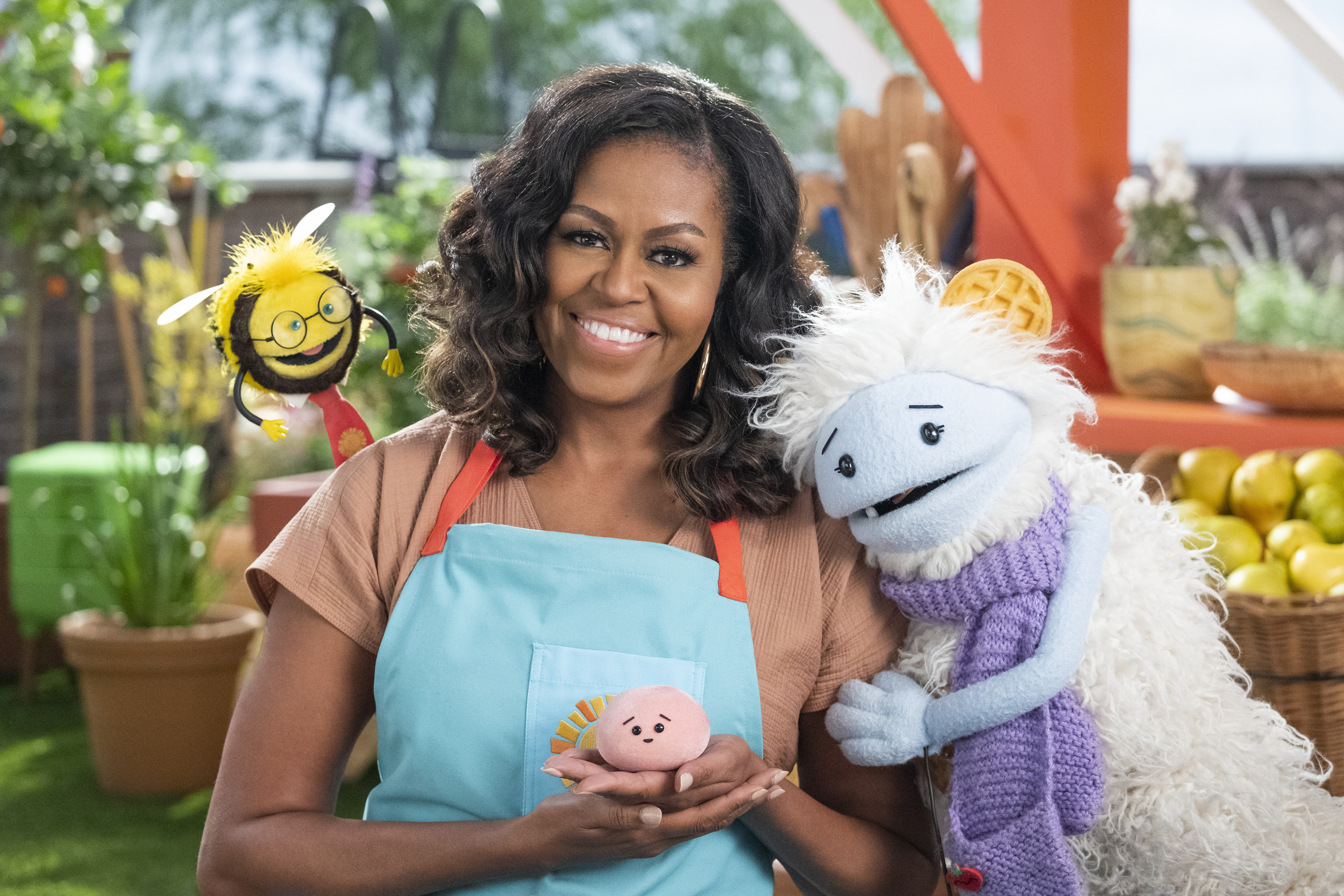 Michelle Obama smiling and holding a mochi stuffie, being hugged by a Muppet-like creature Waffles.