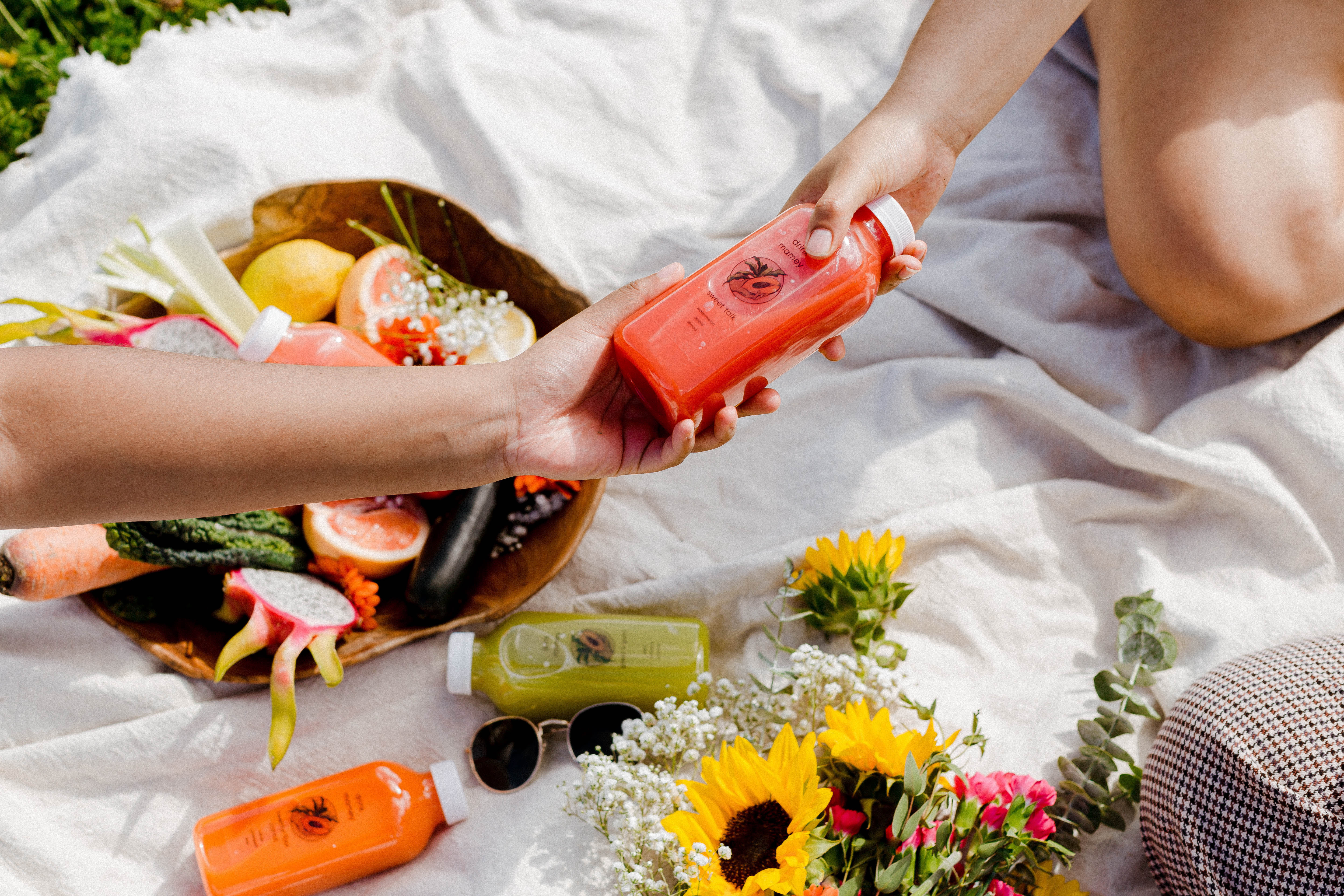 Drink Mamey juices are handed between two people sitting on a blanket at a picnic