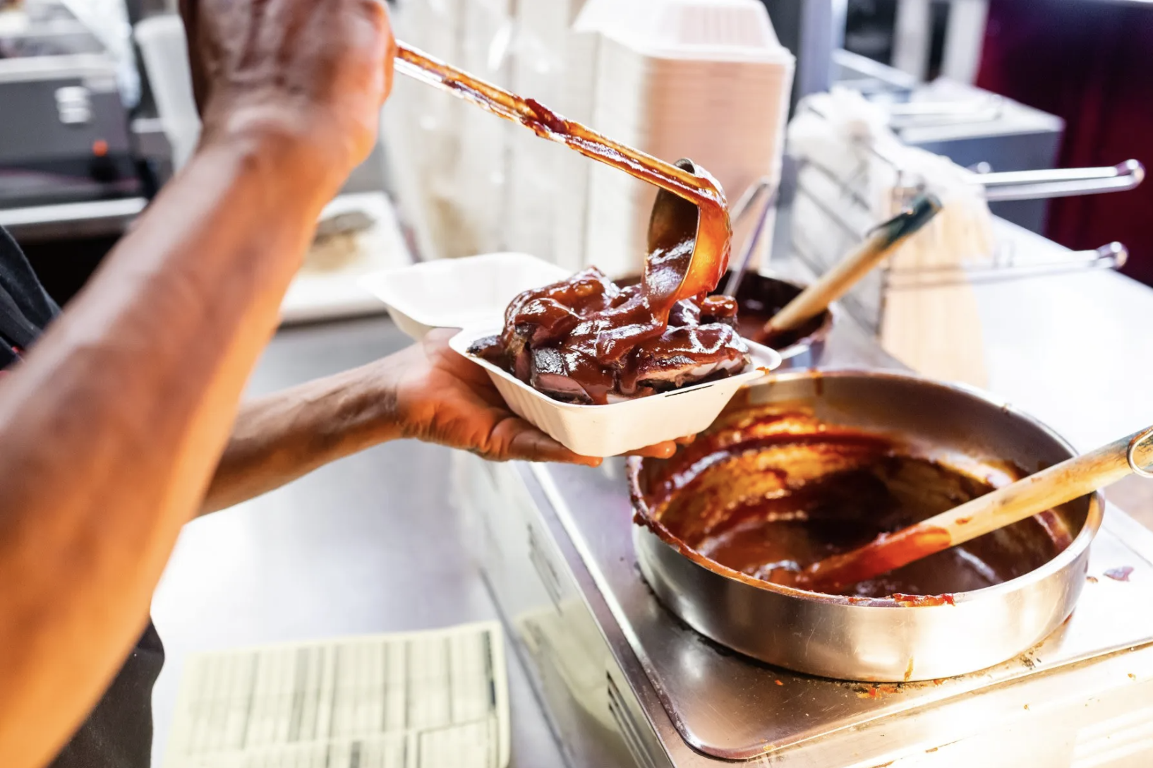 A restaurant worker pours barbecue sauce on top of meat.