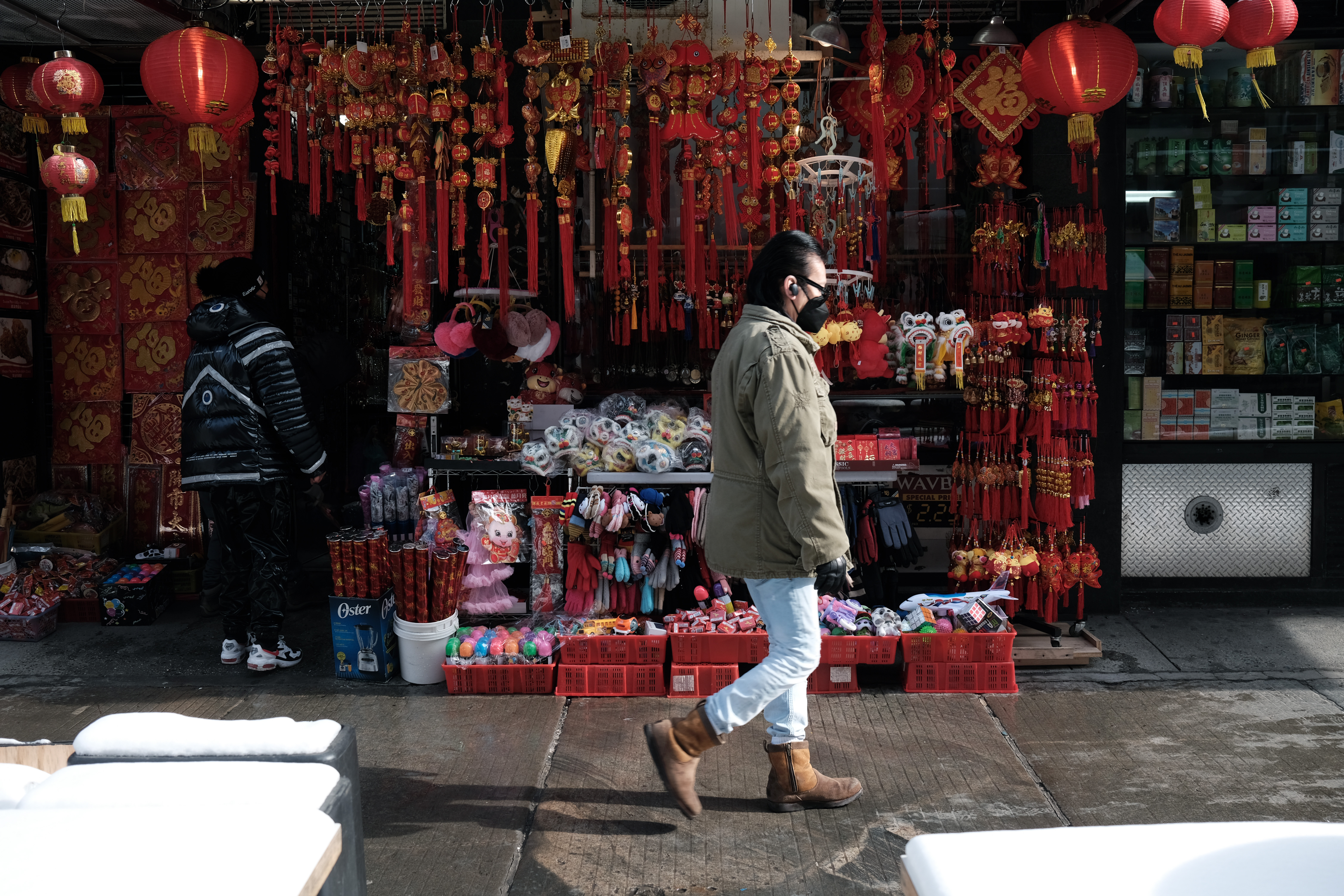 Man wearing mask walks by Chinatown shop with Lunar New Year decorations displayed.
