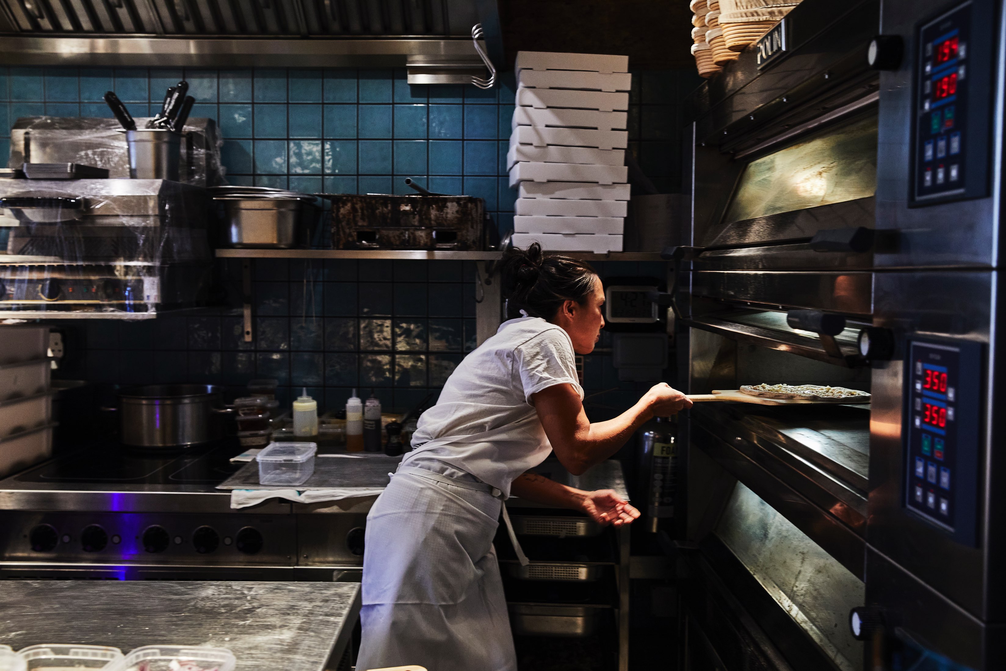 Pam Yung of ASAP pizza, at Flor, slides a pizza into a deck oven using a wooden peel