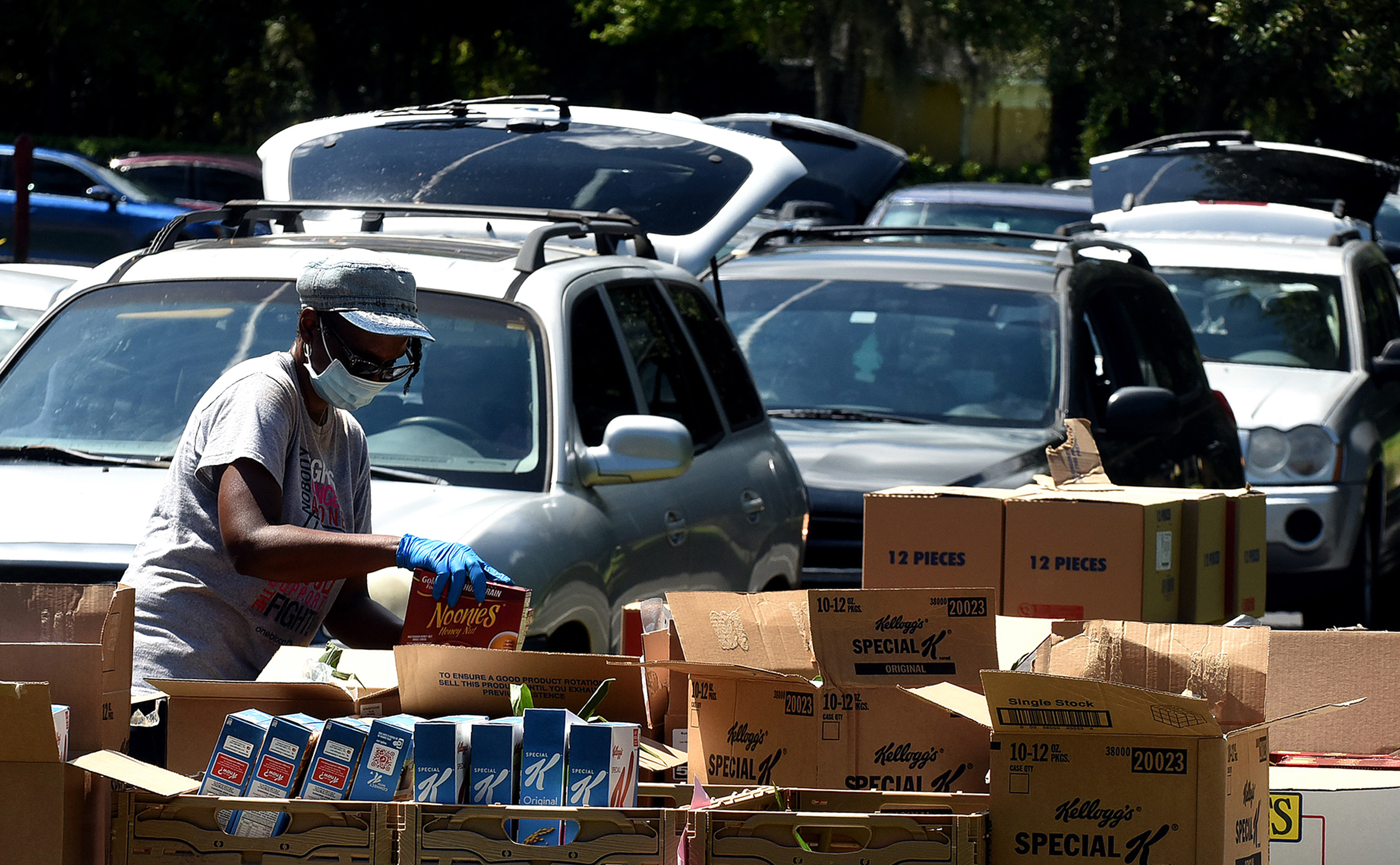 A food bank distribution worker loads boxes beside a line of cars.
