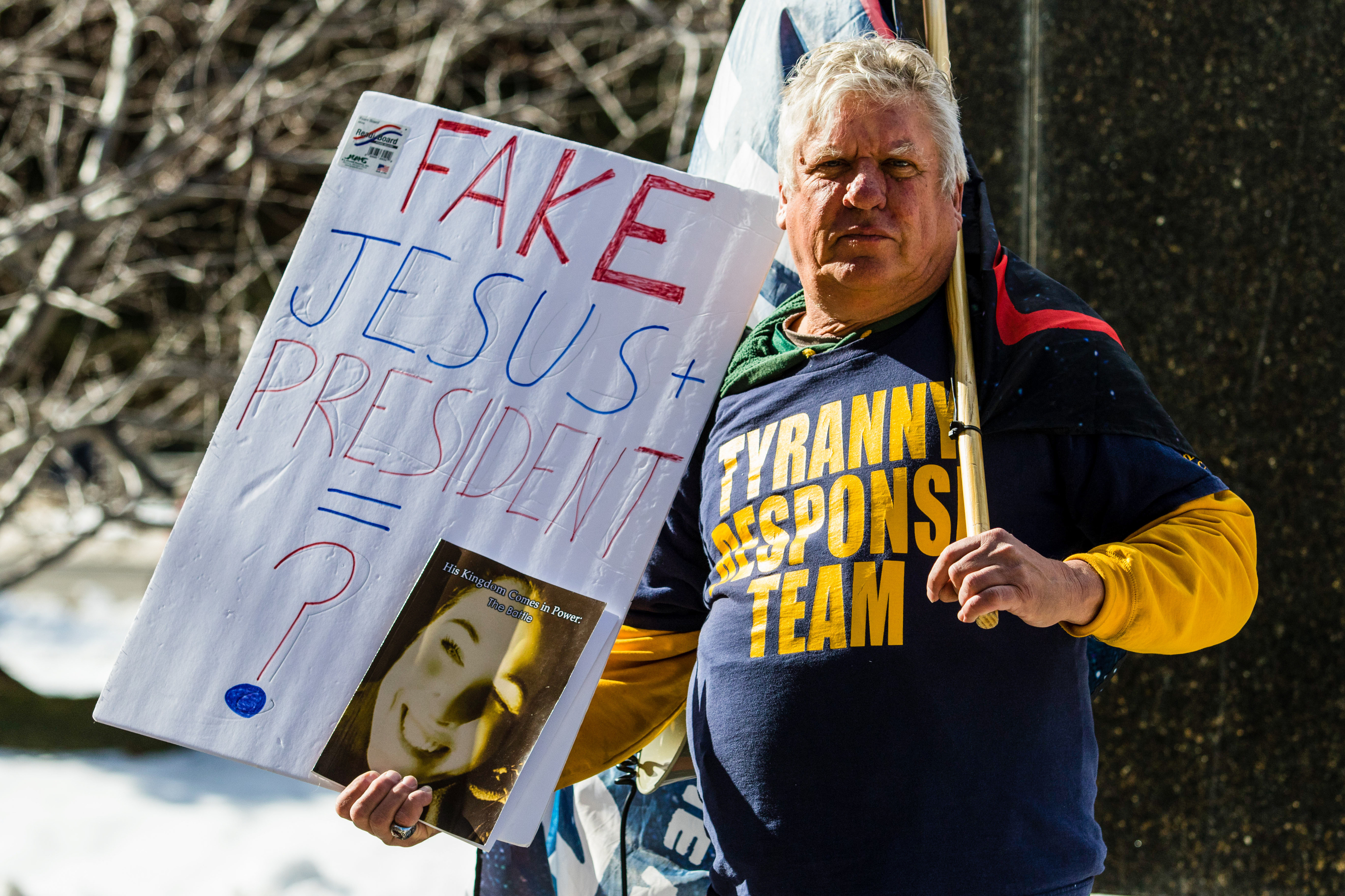 A person in a “Tyranny response team” T-shirt holds a handmade sign that reads “Fake Jesus plus president equals ?”