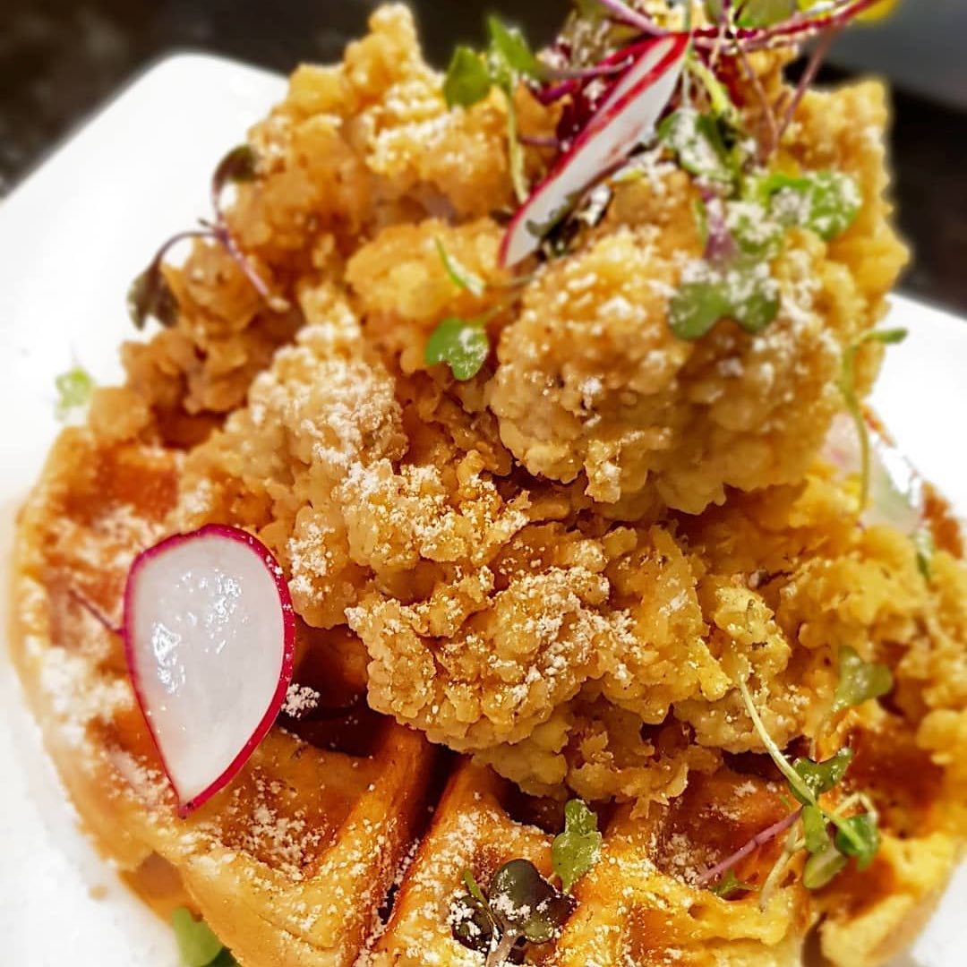 a pile of fried conch fritters on a wafffle, topped with shaved radishes and microgreens