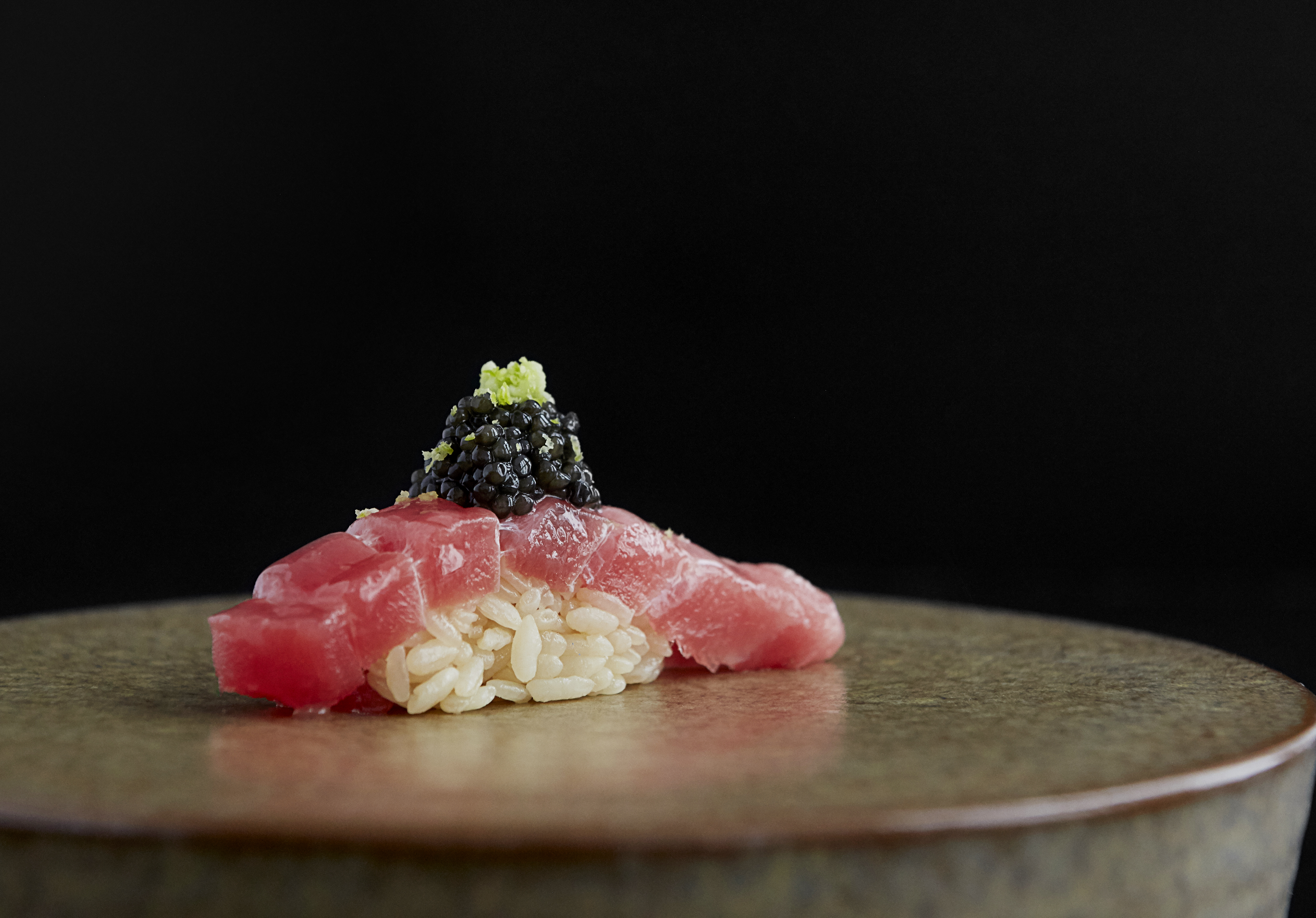 piece of tuna over rice topped with caviar on a plate with a black background
