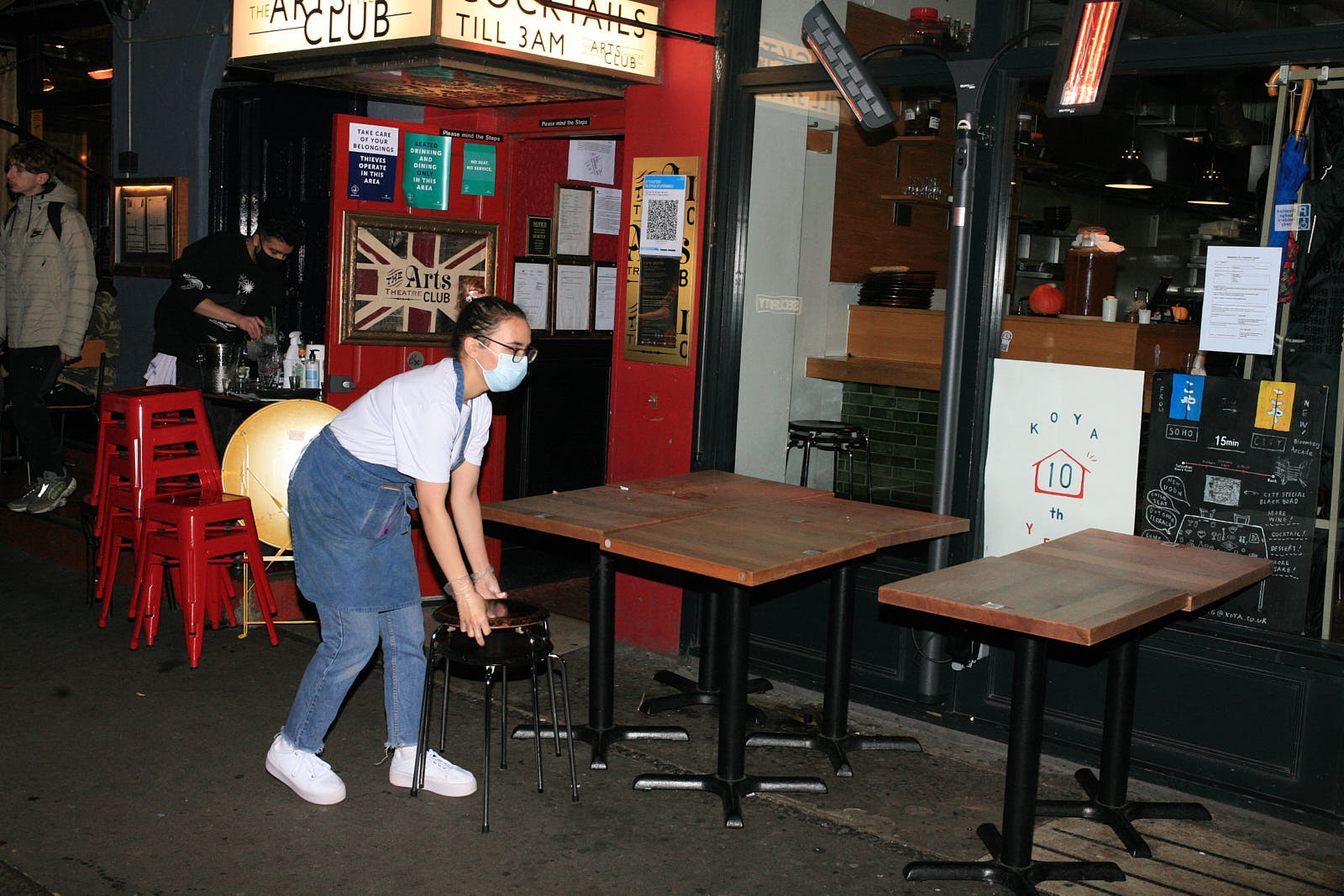 A staff member in a mask moves tables outside Koya restaurant in Soho