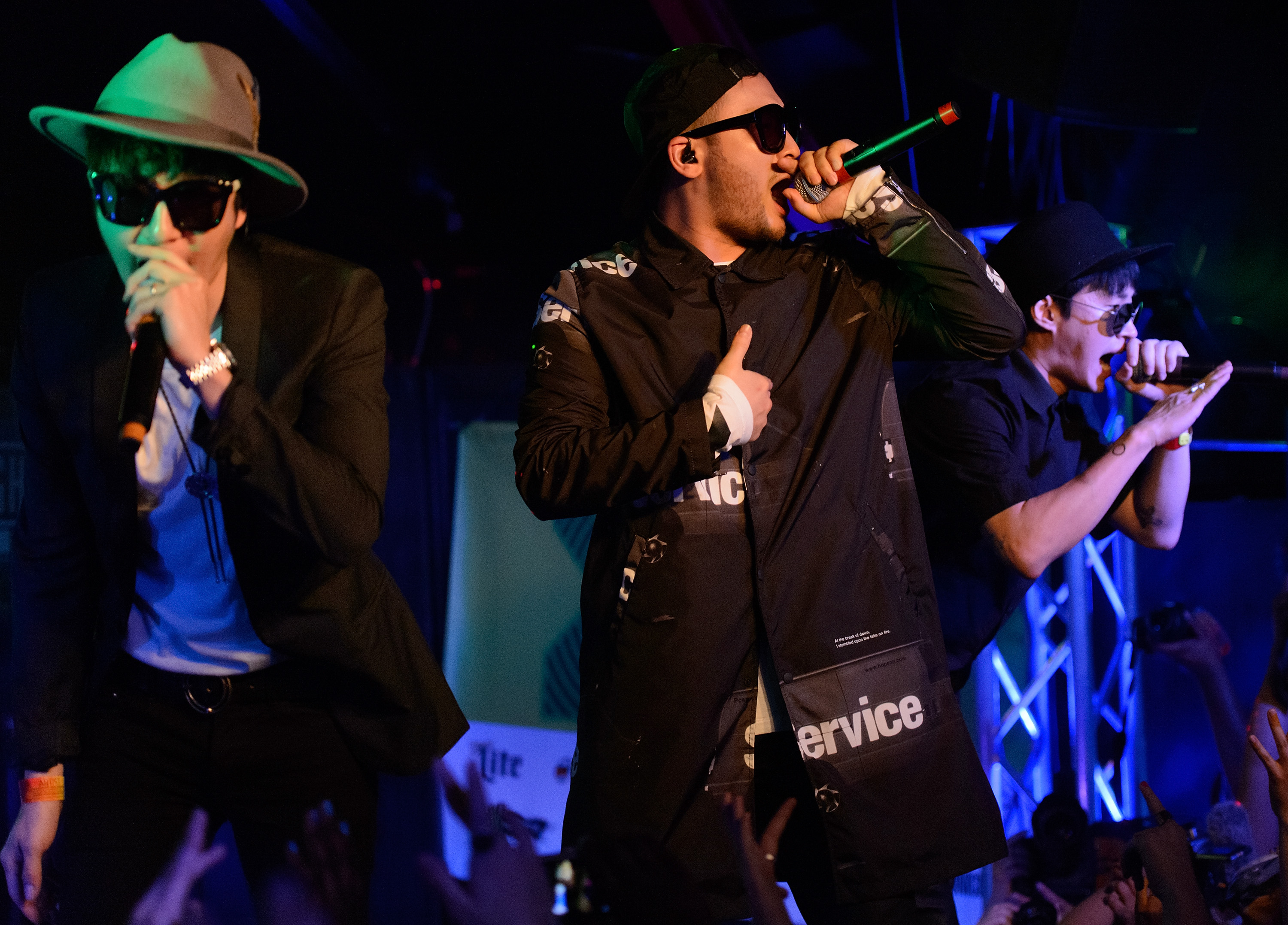 Epik High’s DJ Tukutz, Mithra Jin, and Tablo hold mics and sing on stage.