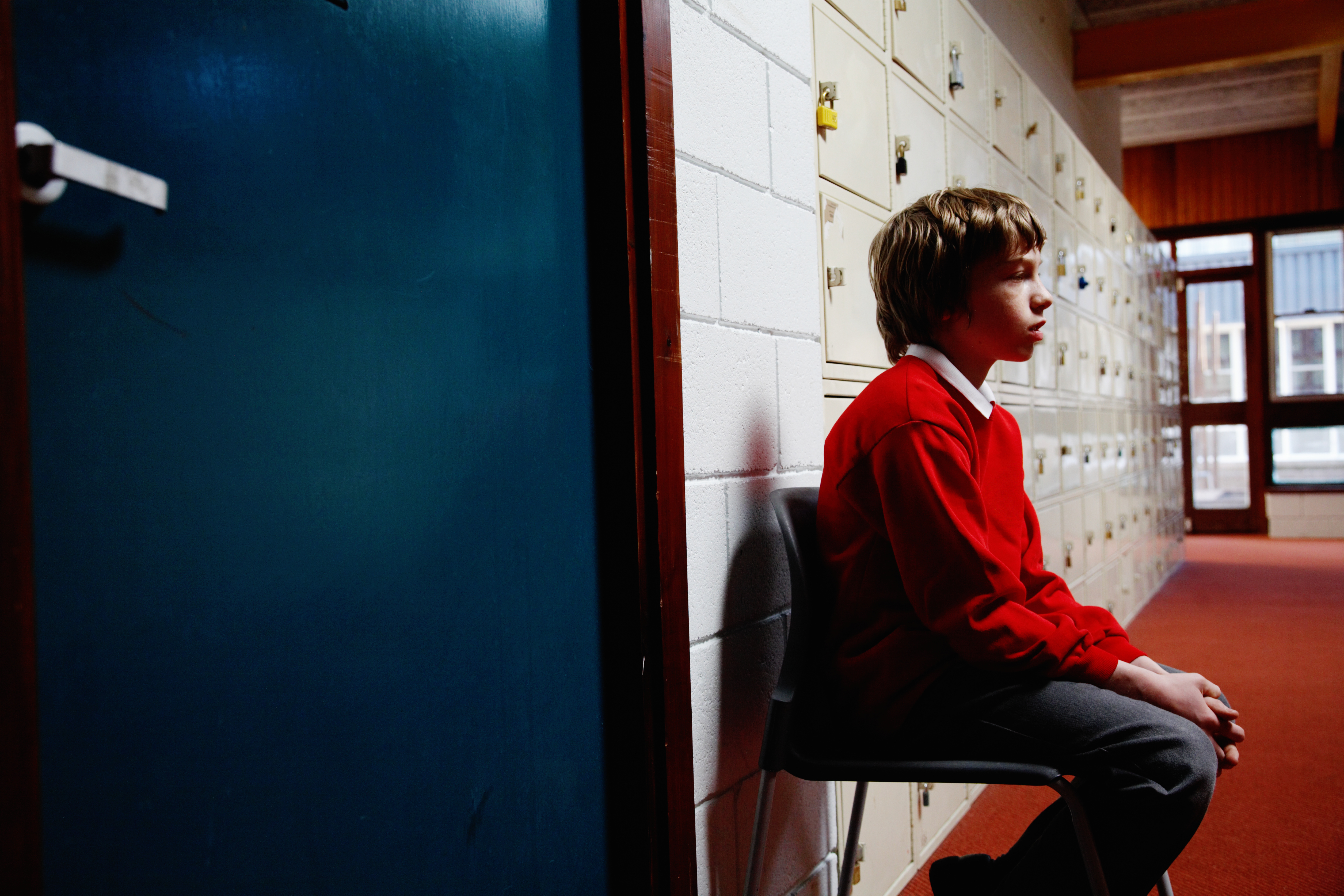 Schoolboy (11-13) sitting on chair in corridor, side view