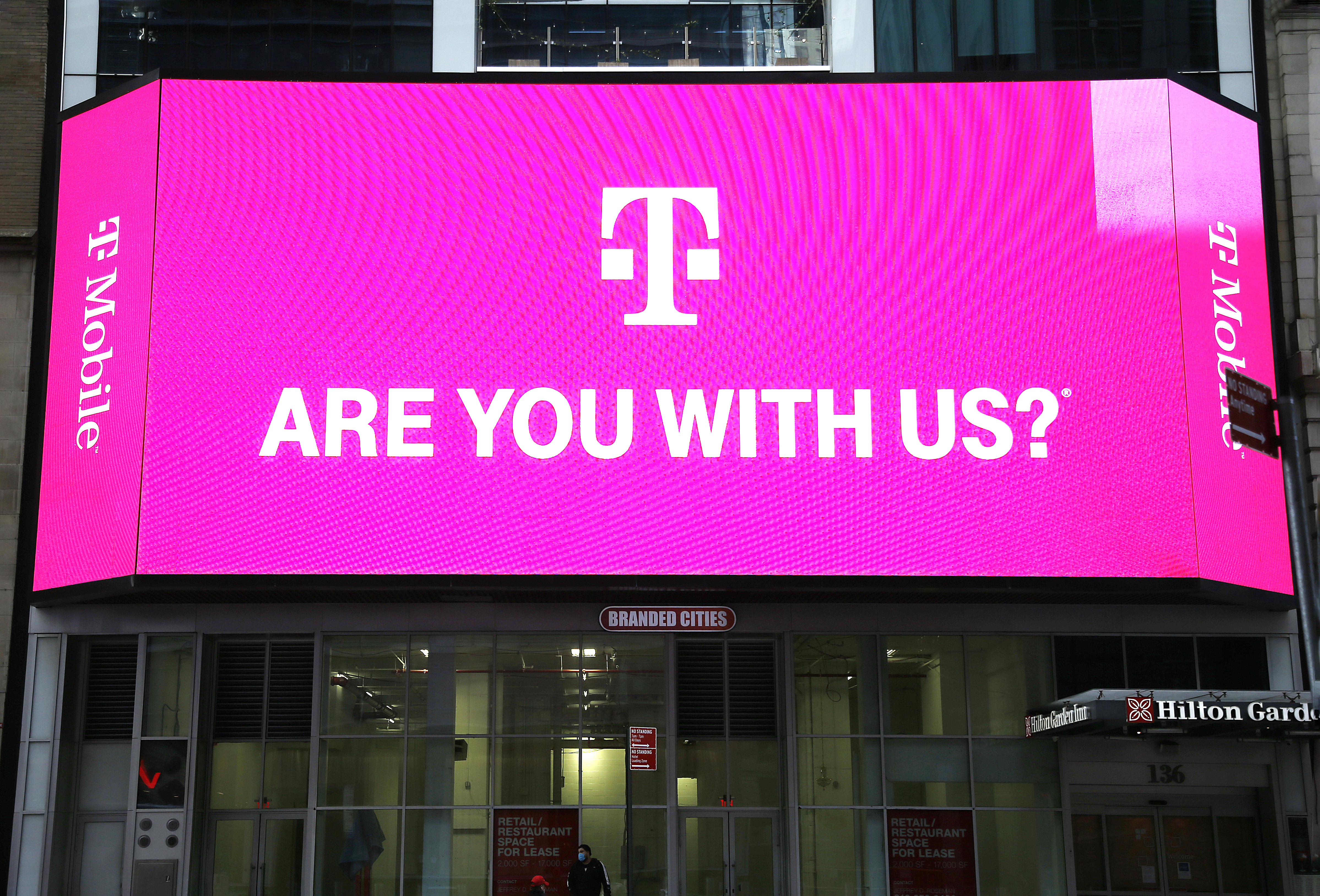 T-Mobile network advertisement seen on a Jumbotron in Times Square reads, “T-Mobile. Are you with us?”