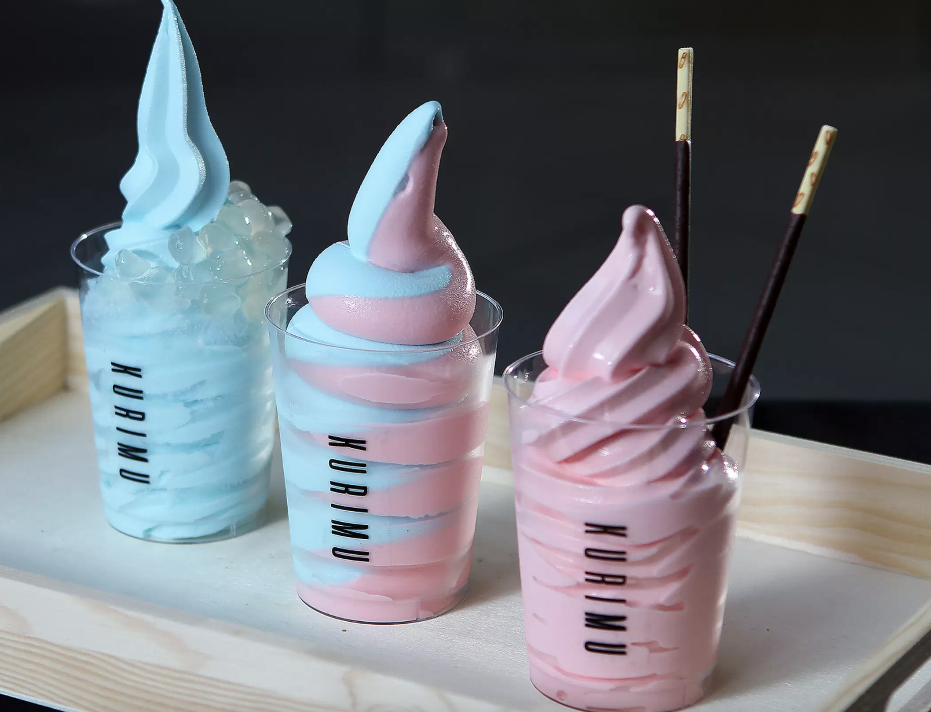 Three clear plastic cups filled with pink and blue soft serve ice cream.