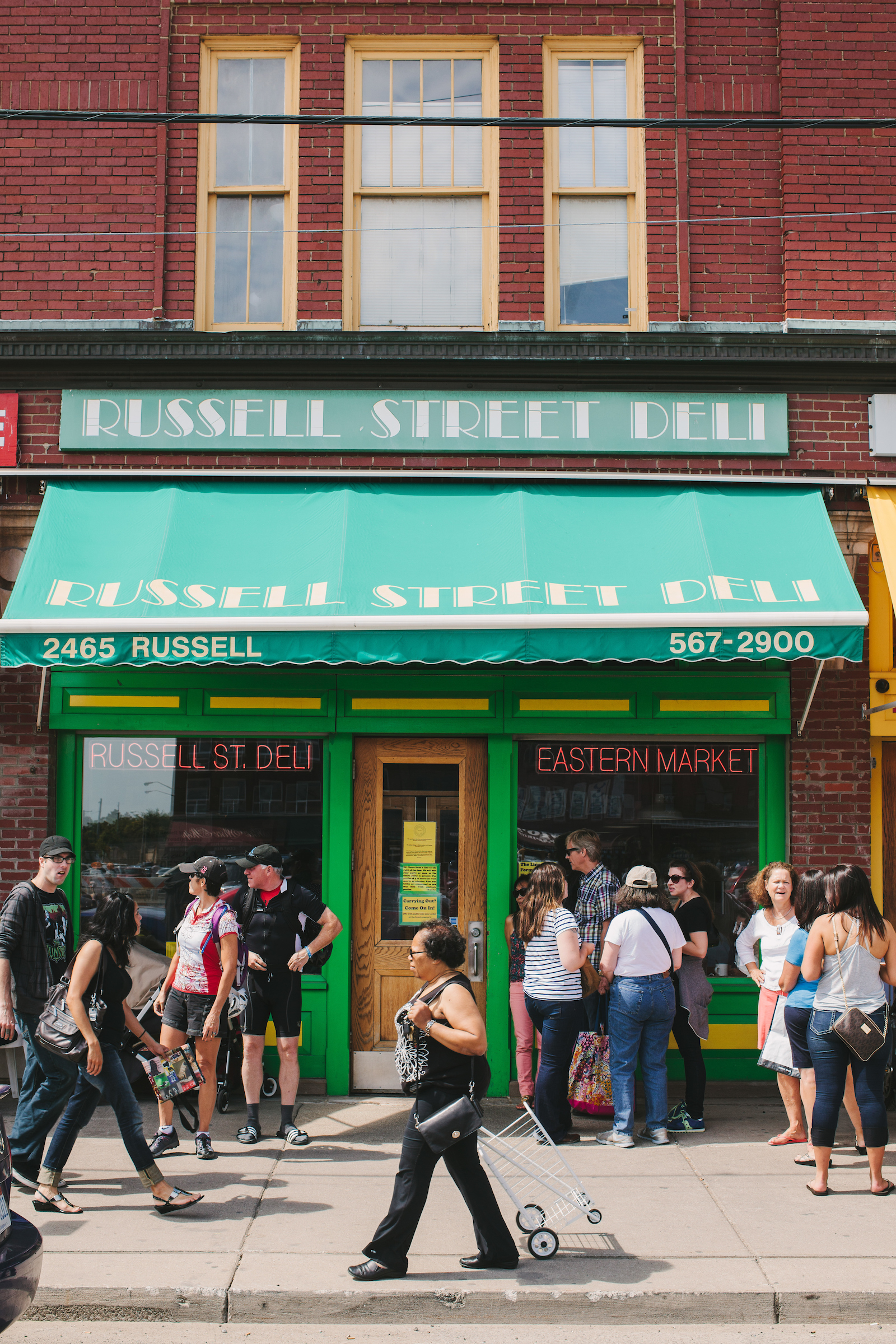Customers gather outside of Russell Street Deli underneath bright green awnings on a sunny day at Eastern Market in Detroit.