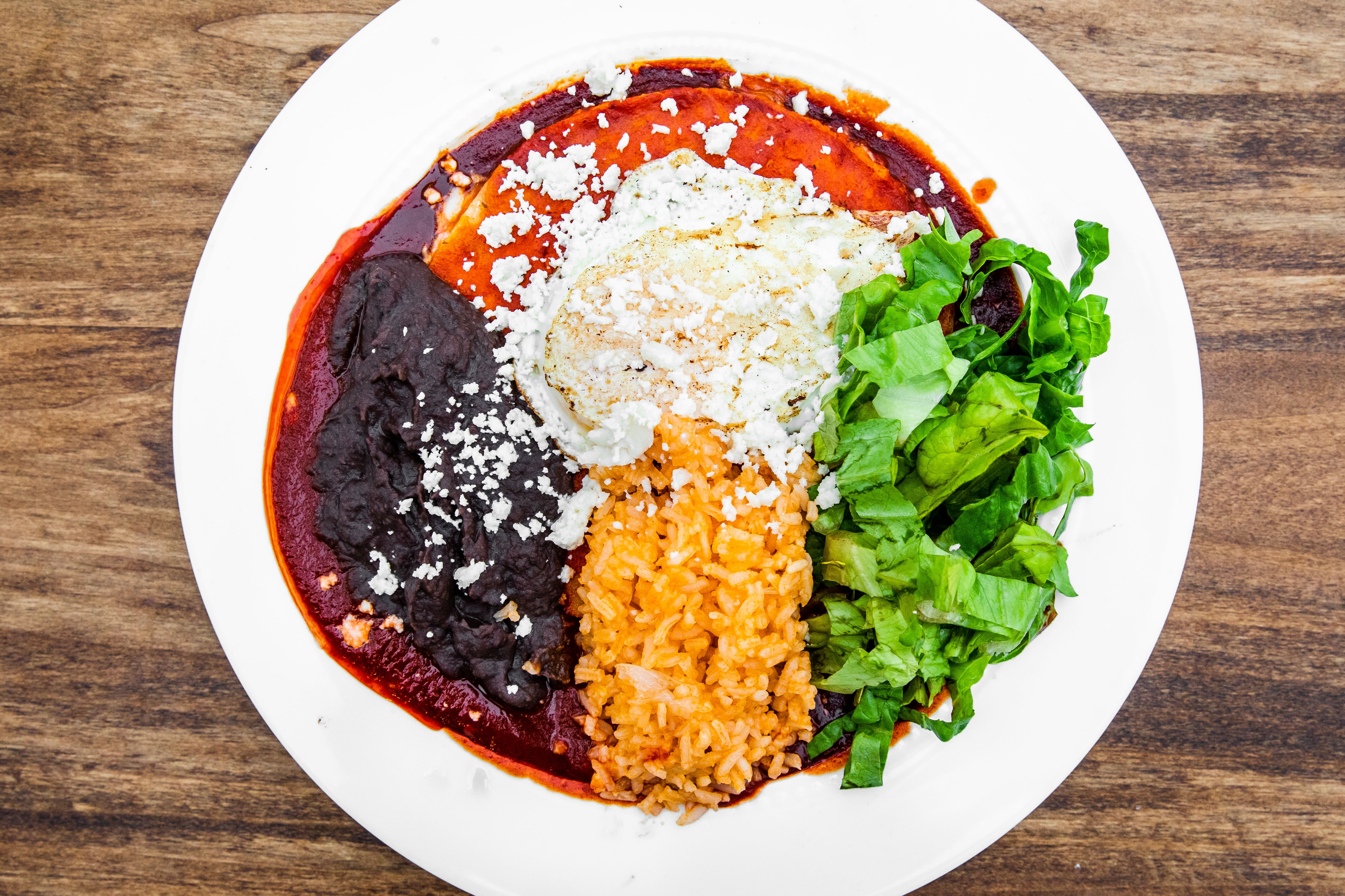 a plate of red chile enchiladas topped with cheese, mexican rice, refried beens and lettuce
