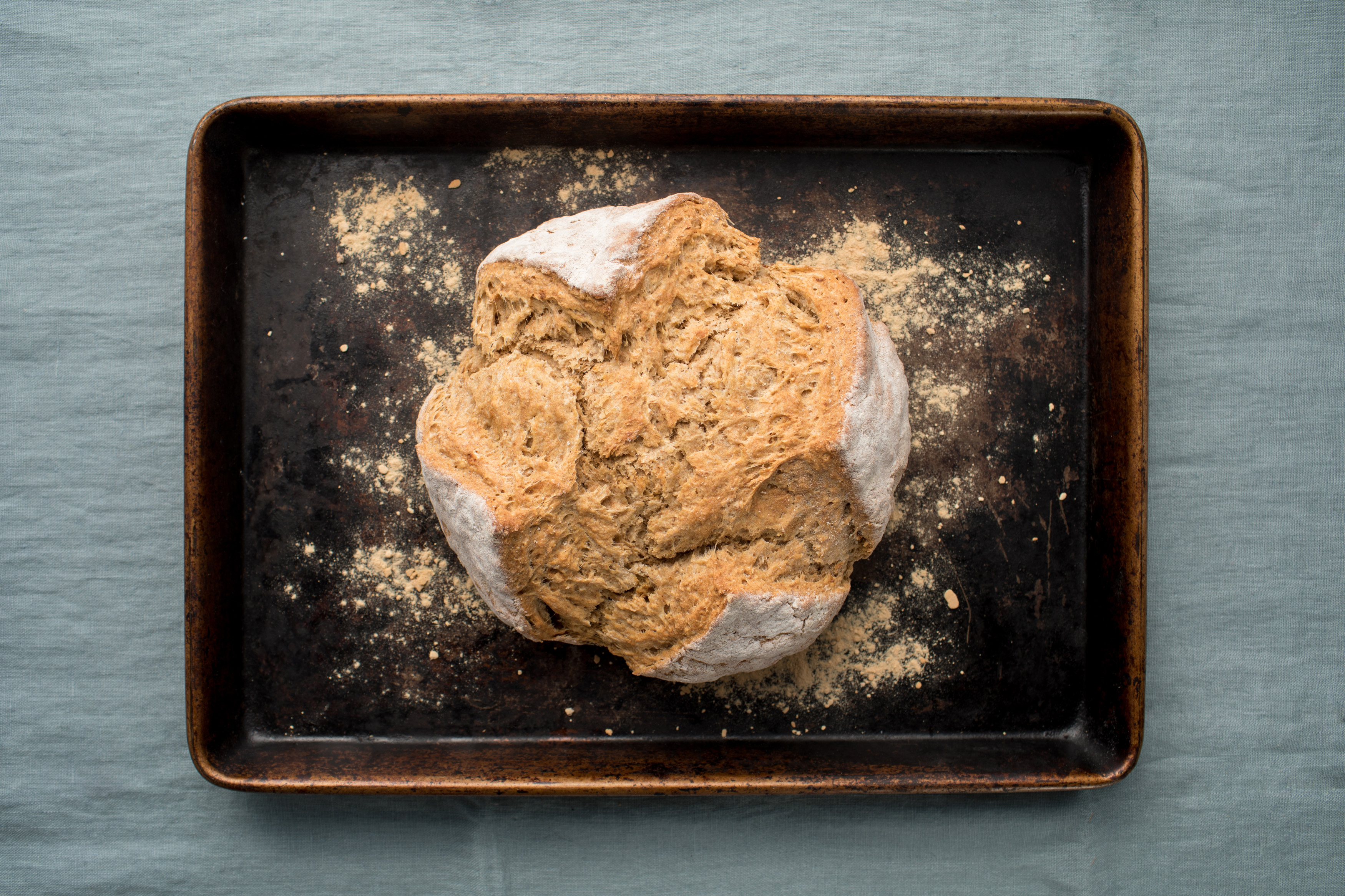 A loaf of soda bread sits on a baking pan atop a blue linen backdrop. 