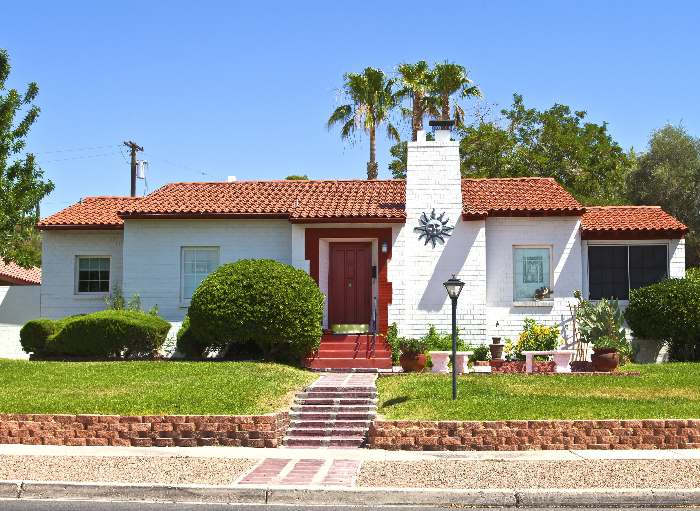 A white home in Nevada with a Spanish roof, red front door, green yard, and planters.