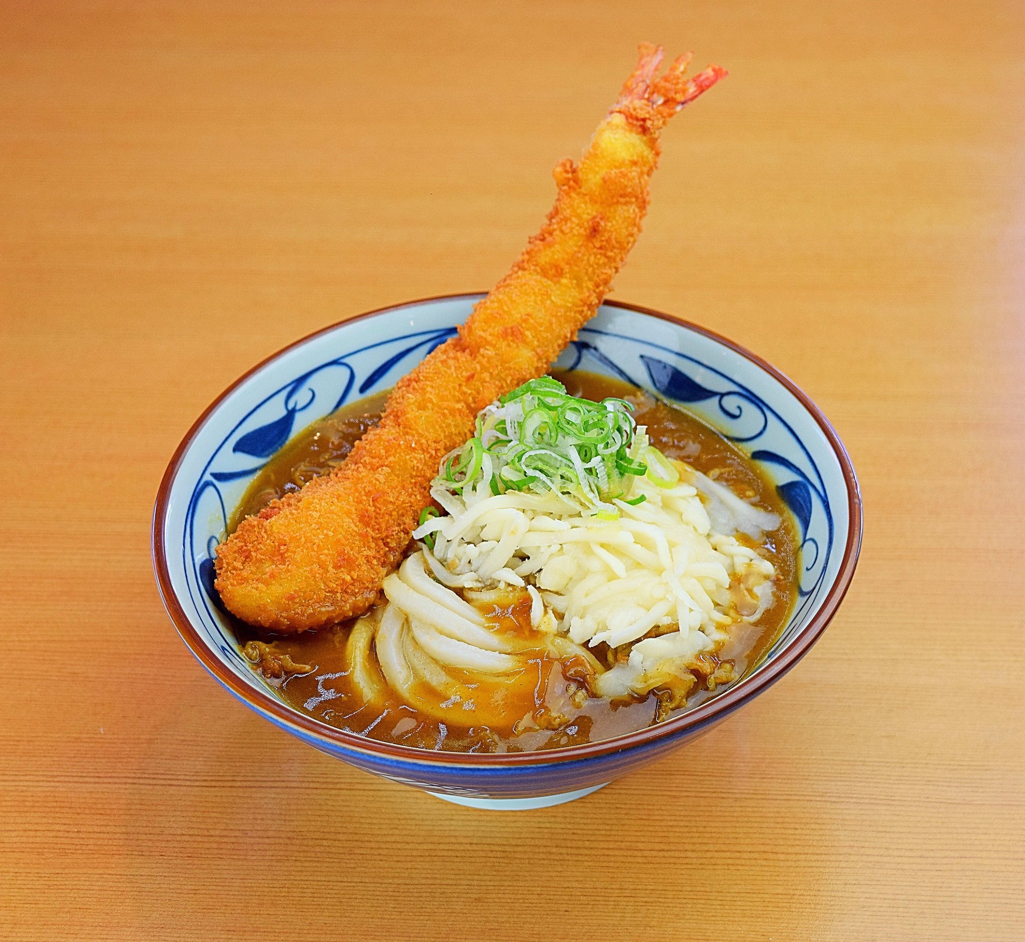A bowl of udon in broth, garnished with a tempura shrimp 