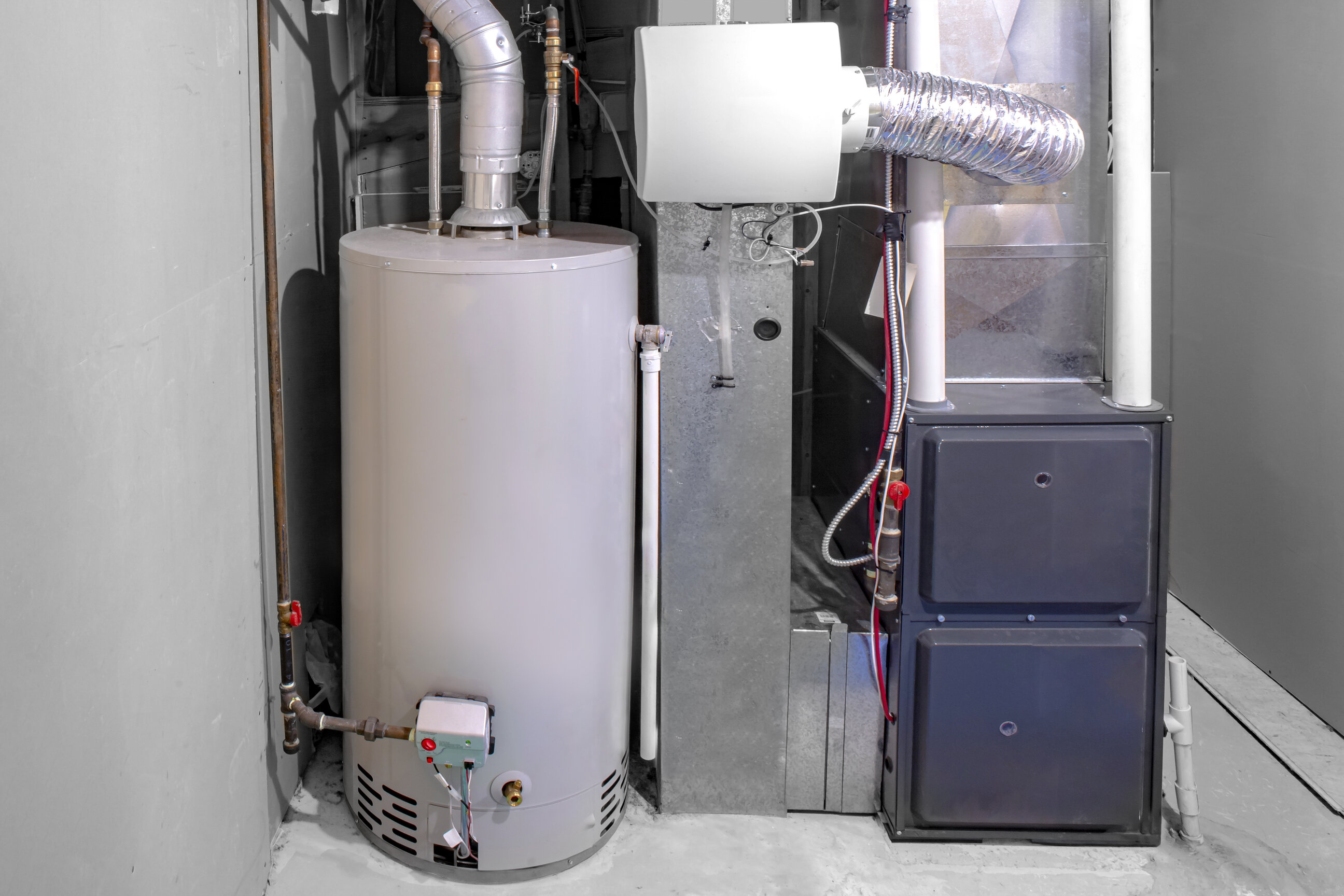 A gray furnace near a water heater and surrounded by other silver-colored home equipment in a gray room.