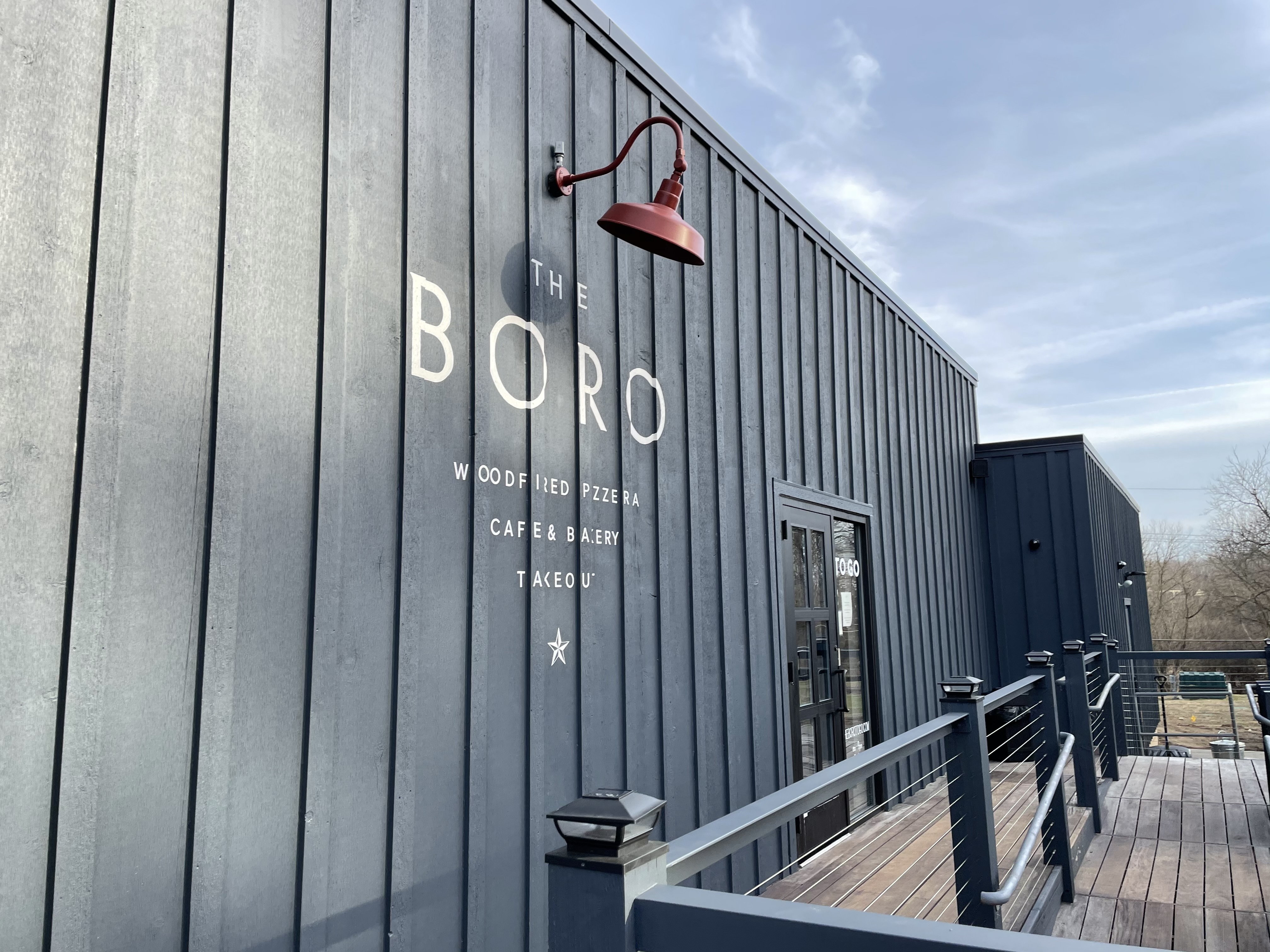 The gray wooden exterior of the Boro in Ann Arbor with the name of the restaurant “The Boro” painted in white letters on the side of the building. A red metal lamp sits above the name to illuminate it at night