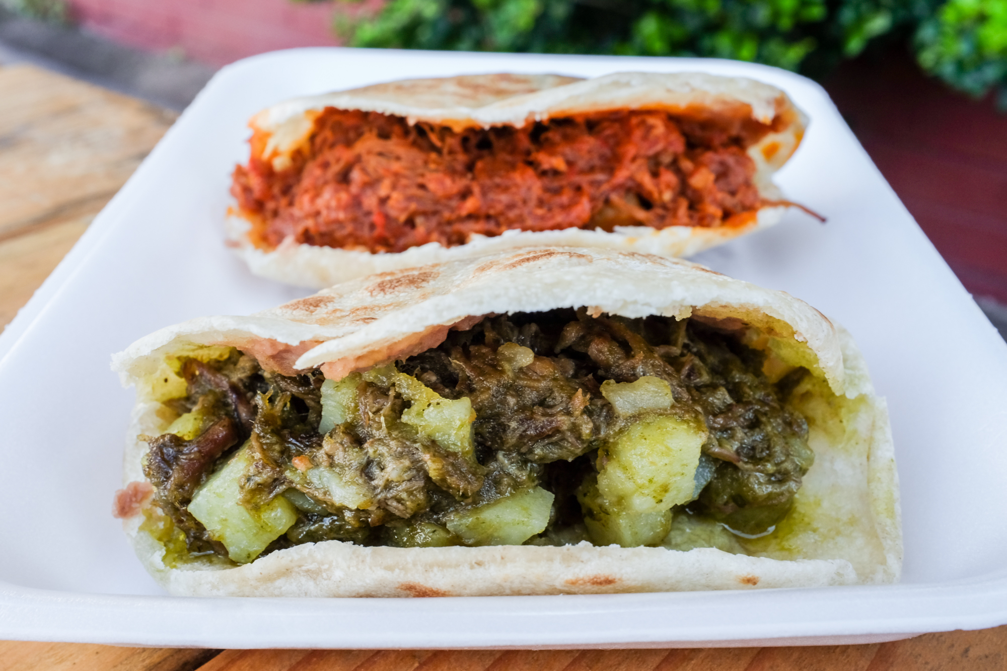 A gordita stuffed with bright red meat and another stuffed with green salsa verde meat and a white rectangular plate.