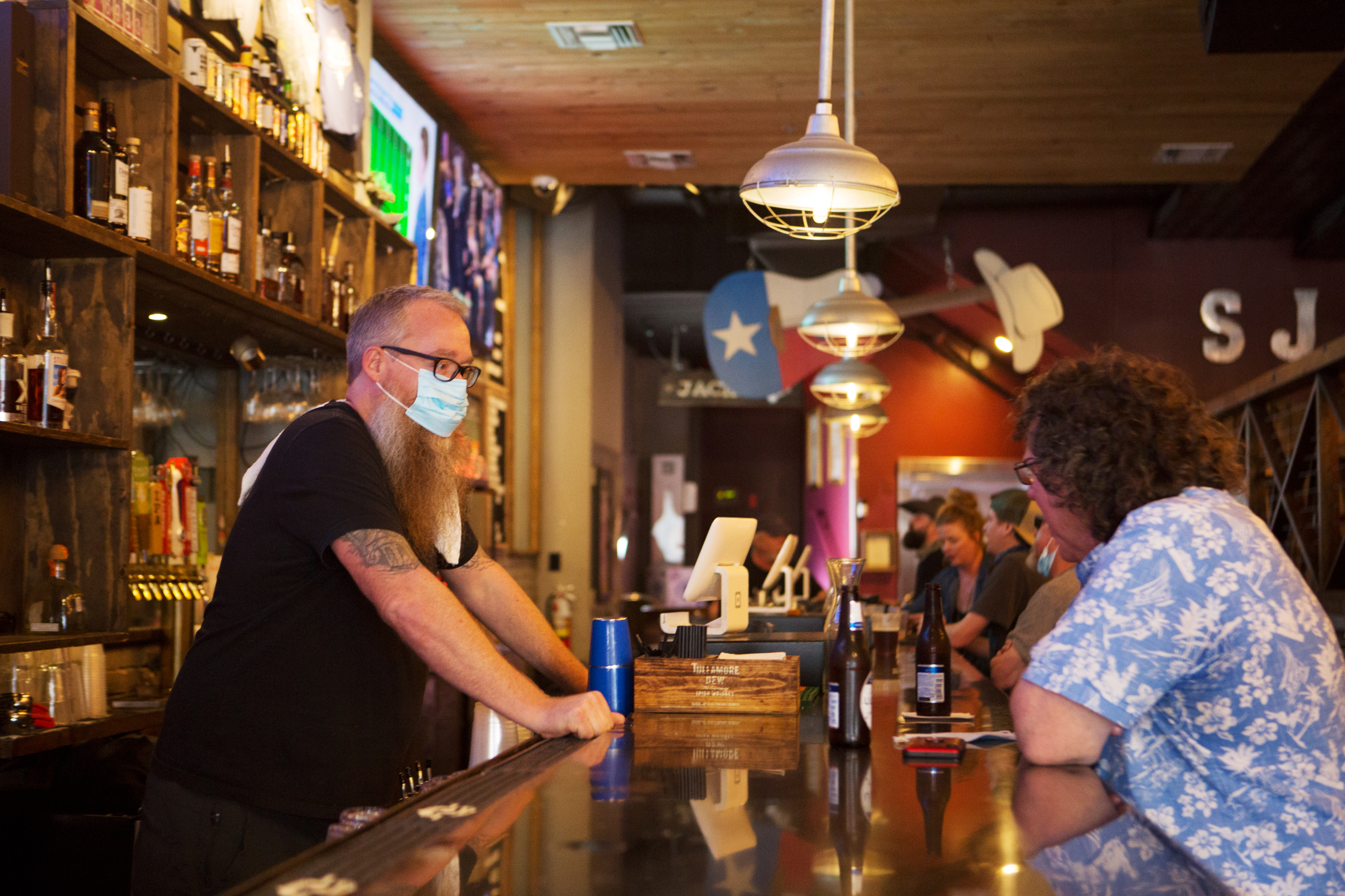 A masked bartender serving a customer at an Austin bar in March