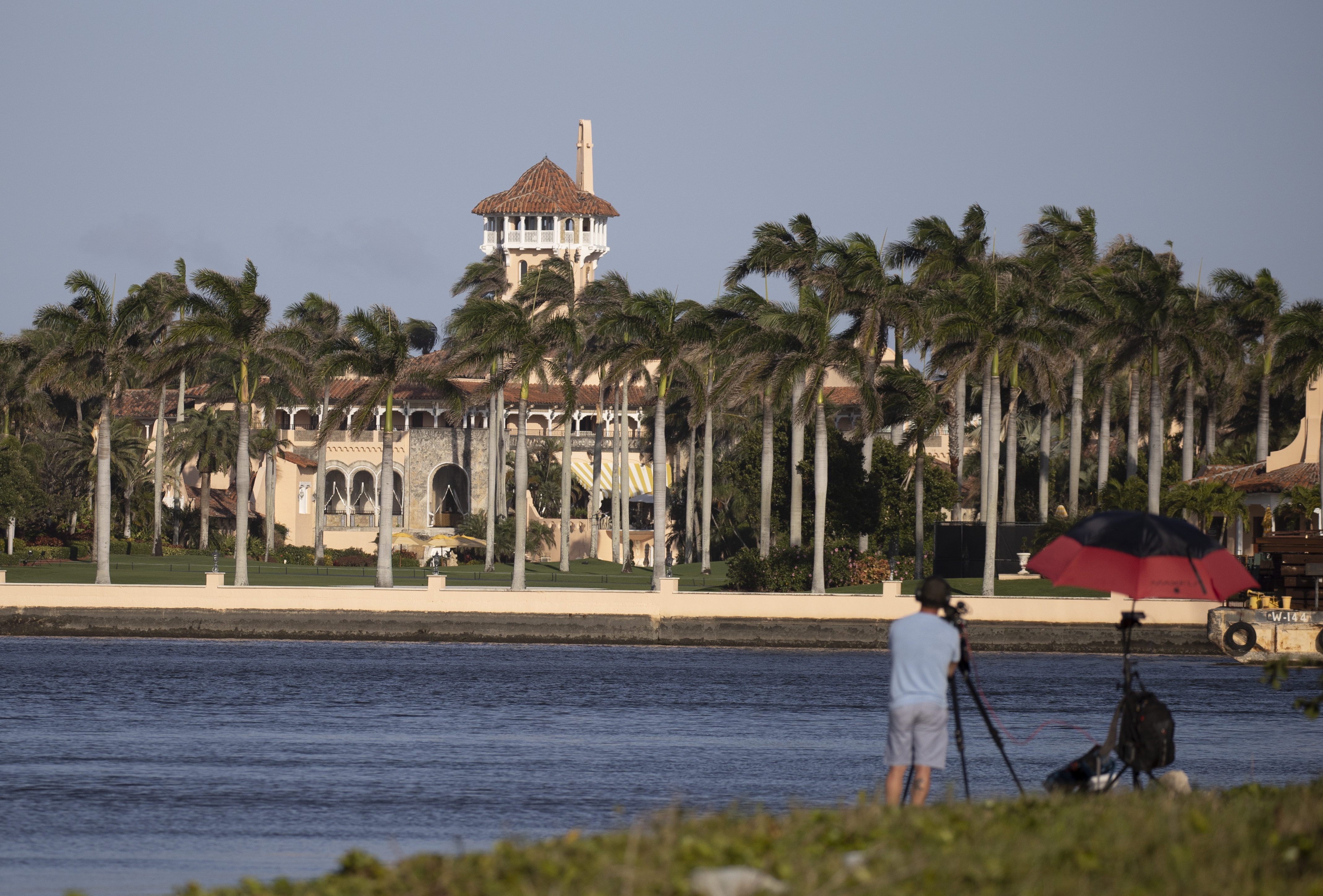 Mar-a-Lago in Palm Beach, Florida, as seen from across the Intracoastal Waterway. A man stands in the foreground with a camera on a tripod.