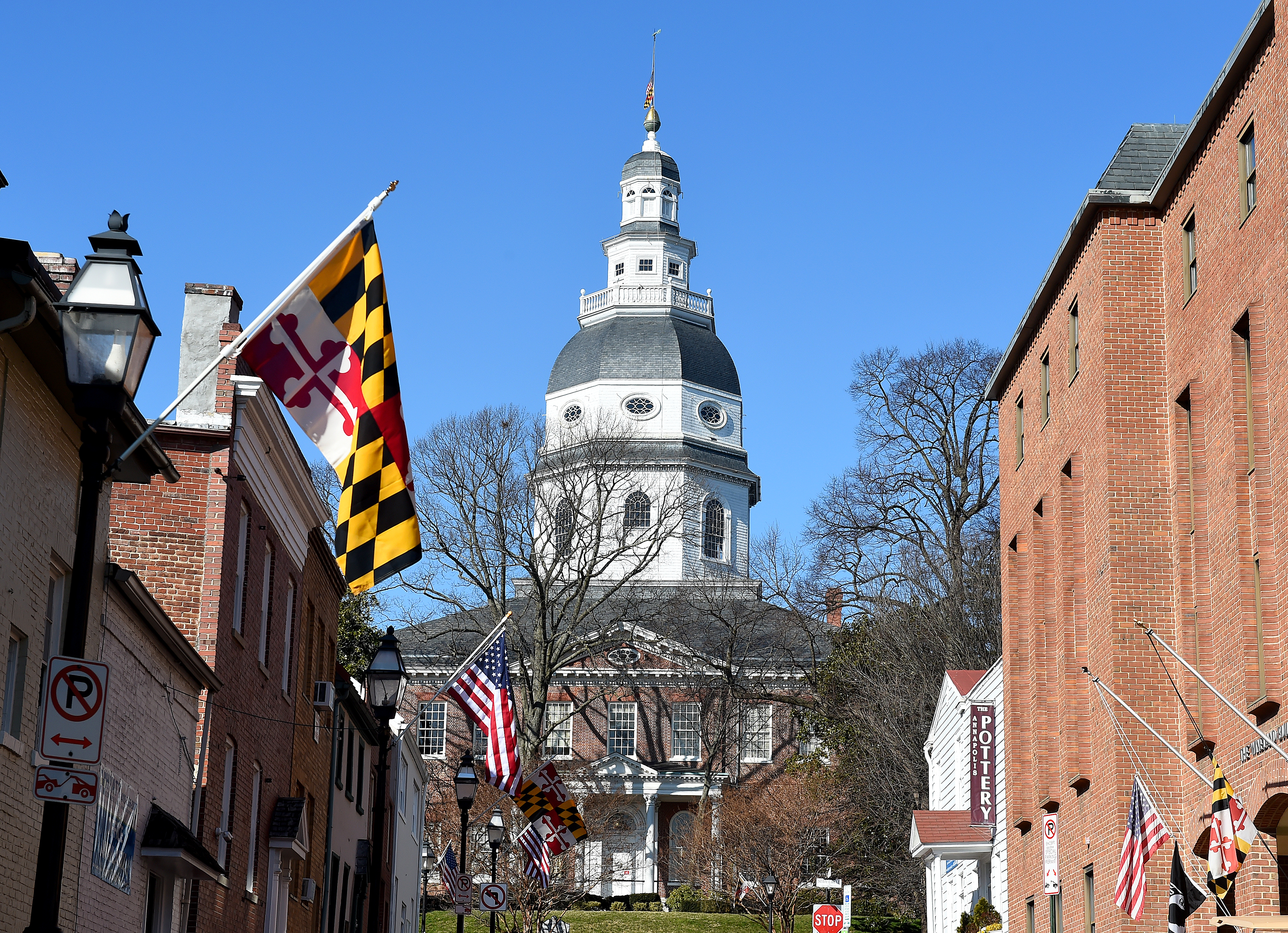 The Maryland State House building is pictured. In the foreground is a Maryland state flag.
