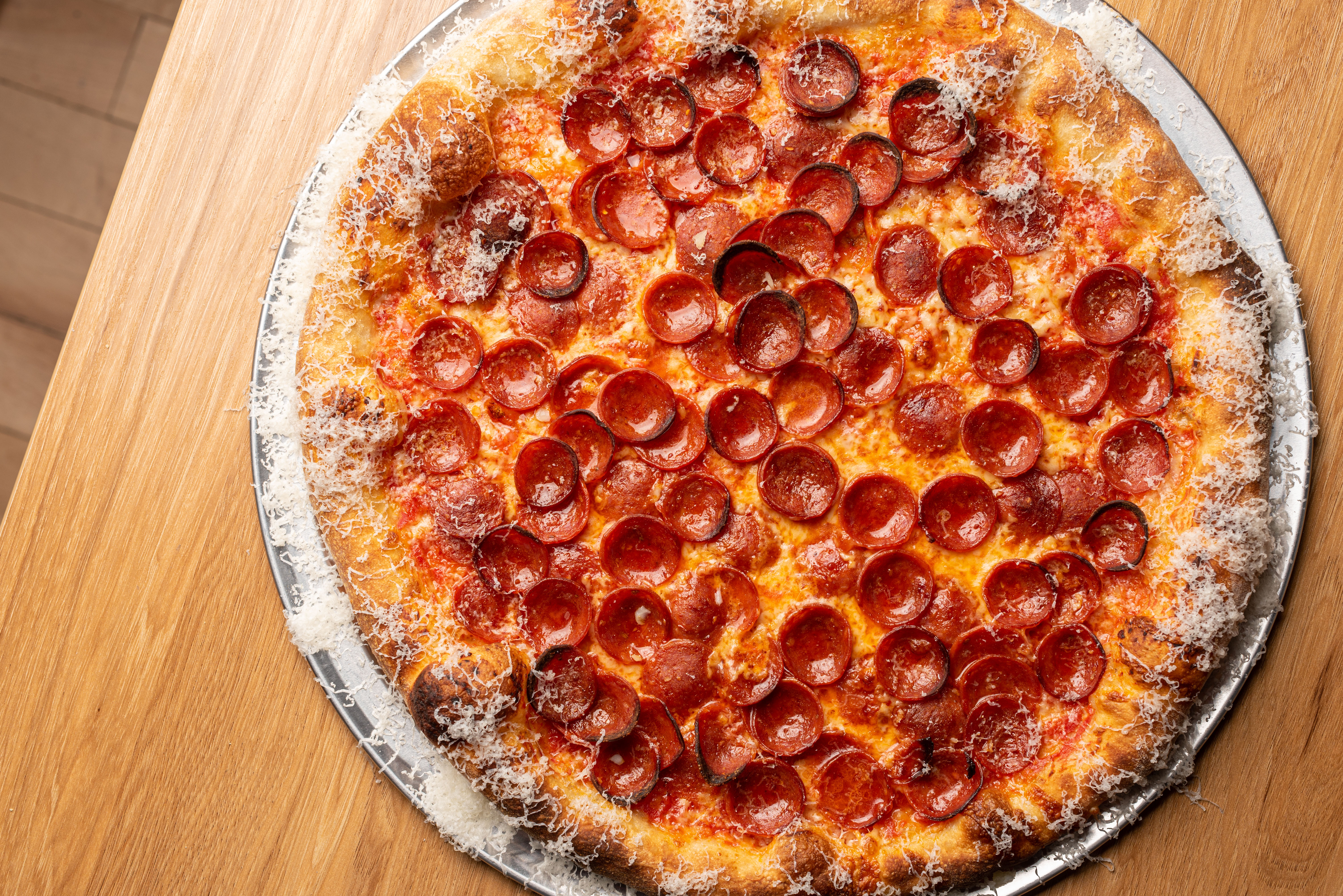 An overhead shot of a pepperoni pizza with cheese shaved onto the crust.