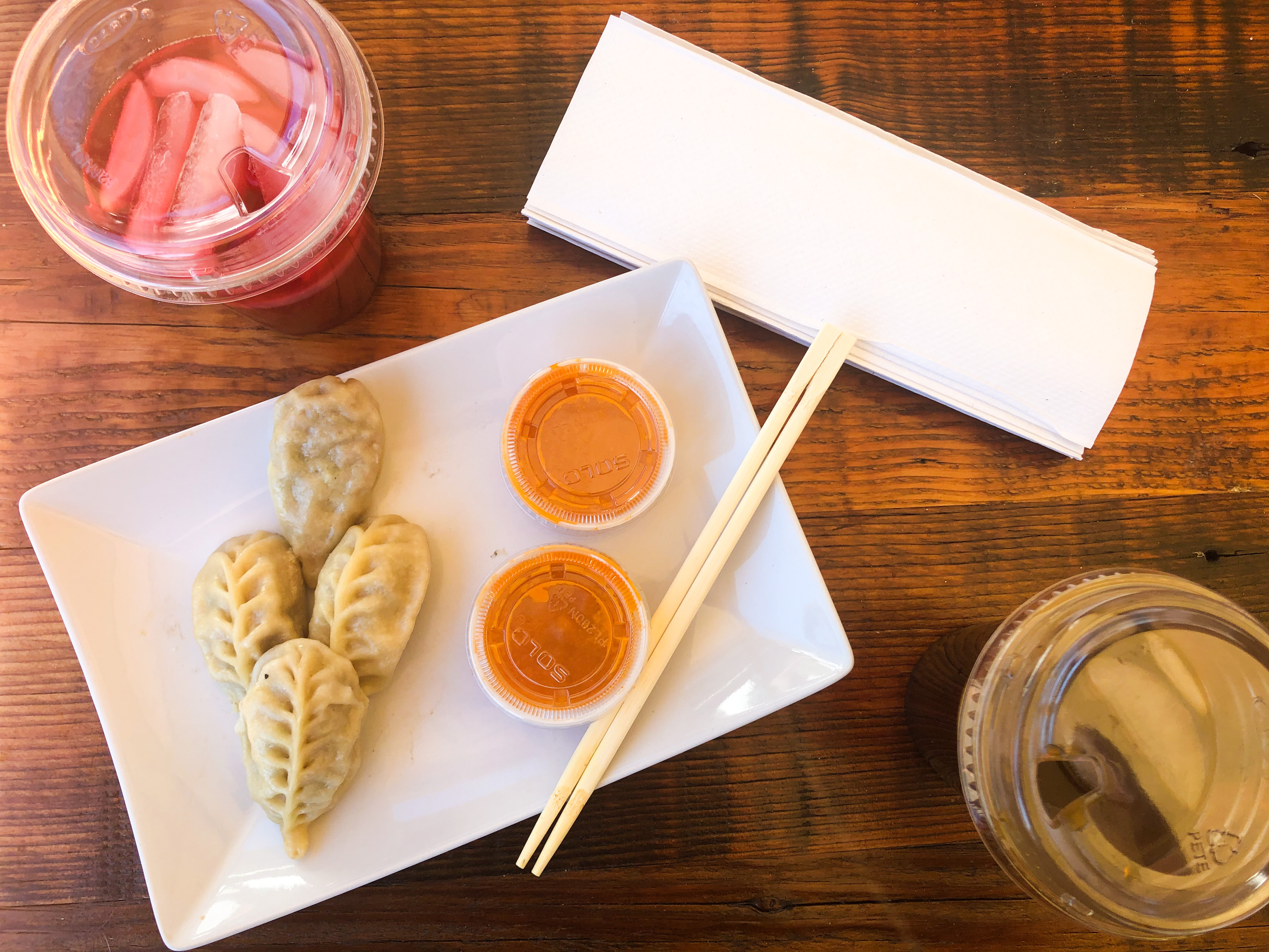 A table with four dumplings on a plate next to two containers of tomato chutney, placed next to hibiscus drinks and Kenyan lemonade