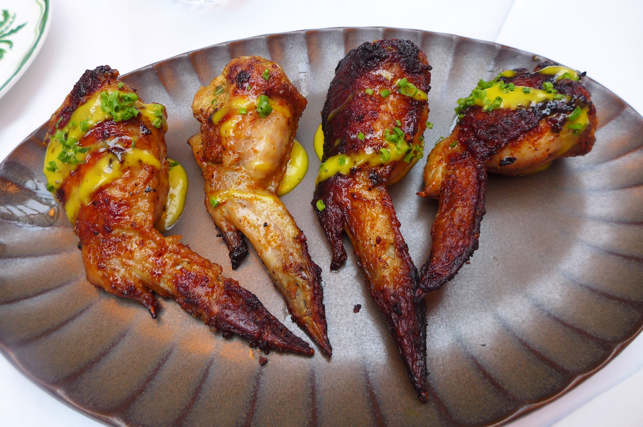Four wings coated with spices on a metallic gray plate with ripples.