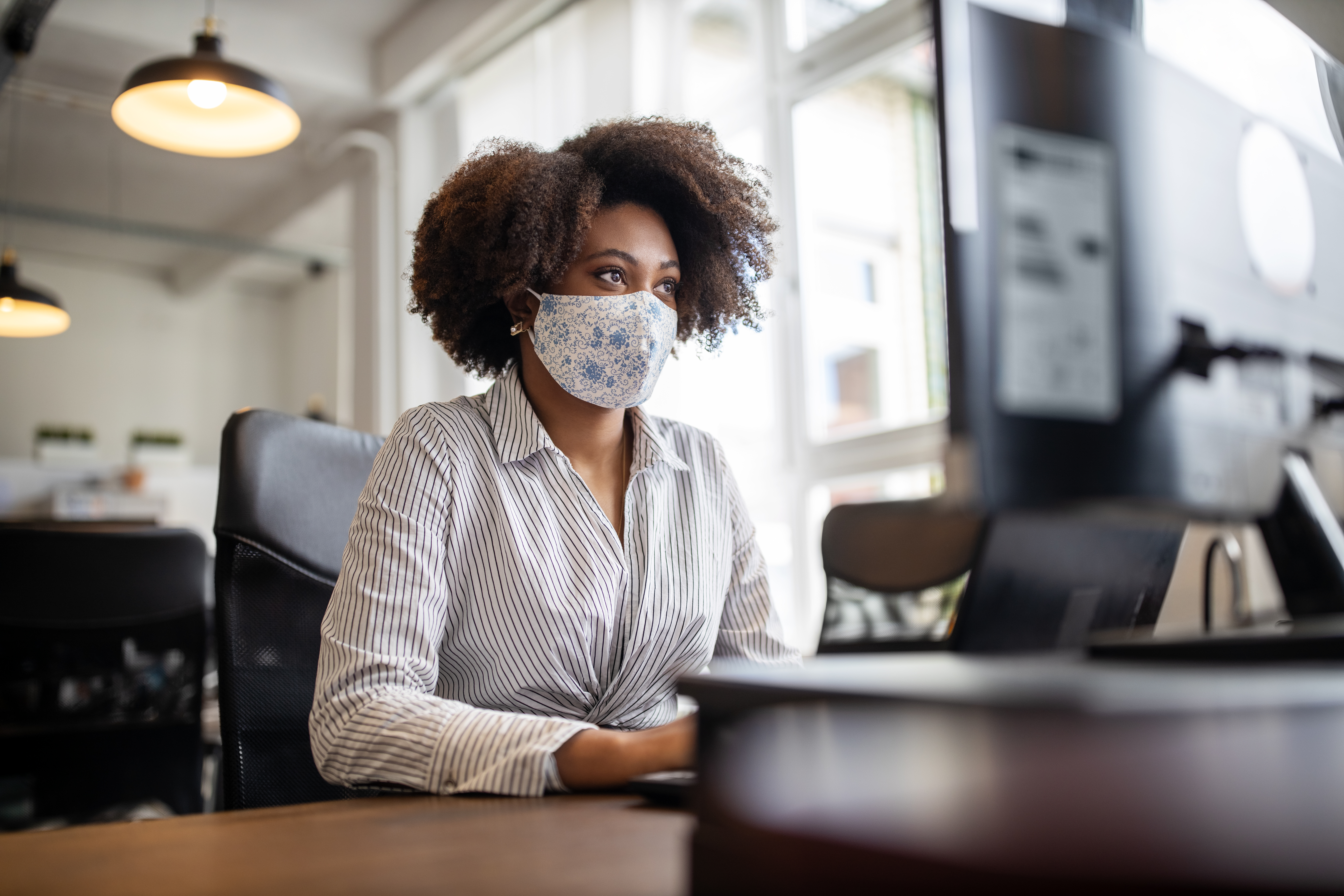 Person wearing a face mask working at a desk looking at computer monitor in an office.