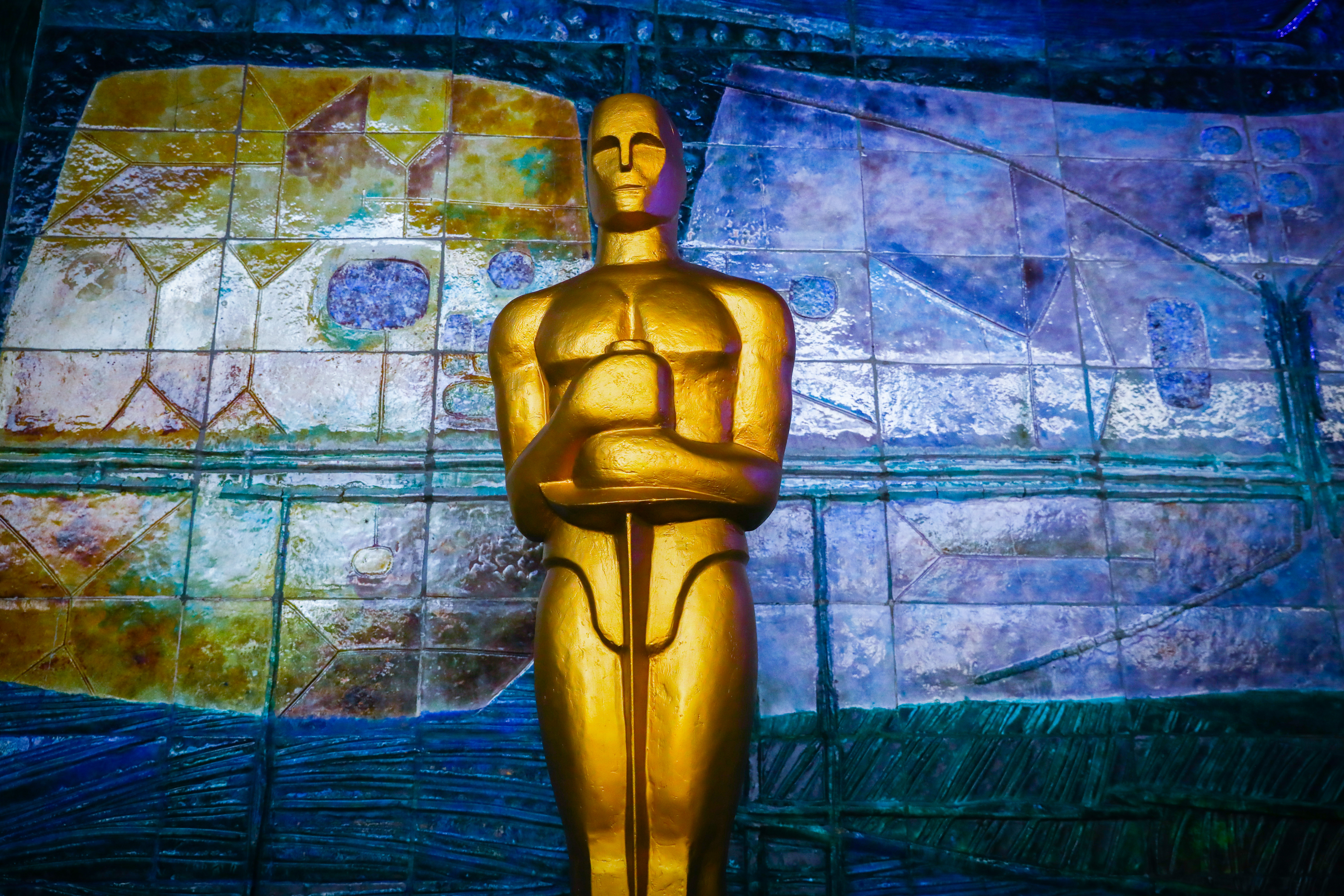 An Oscar statue in front of a colorful background.