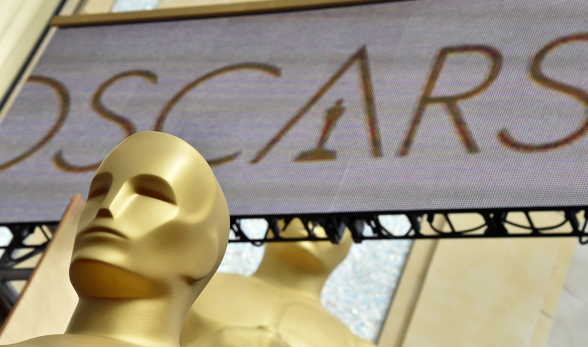 a close-up of a giant Oscar statue with an Oscars sign behind it