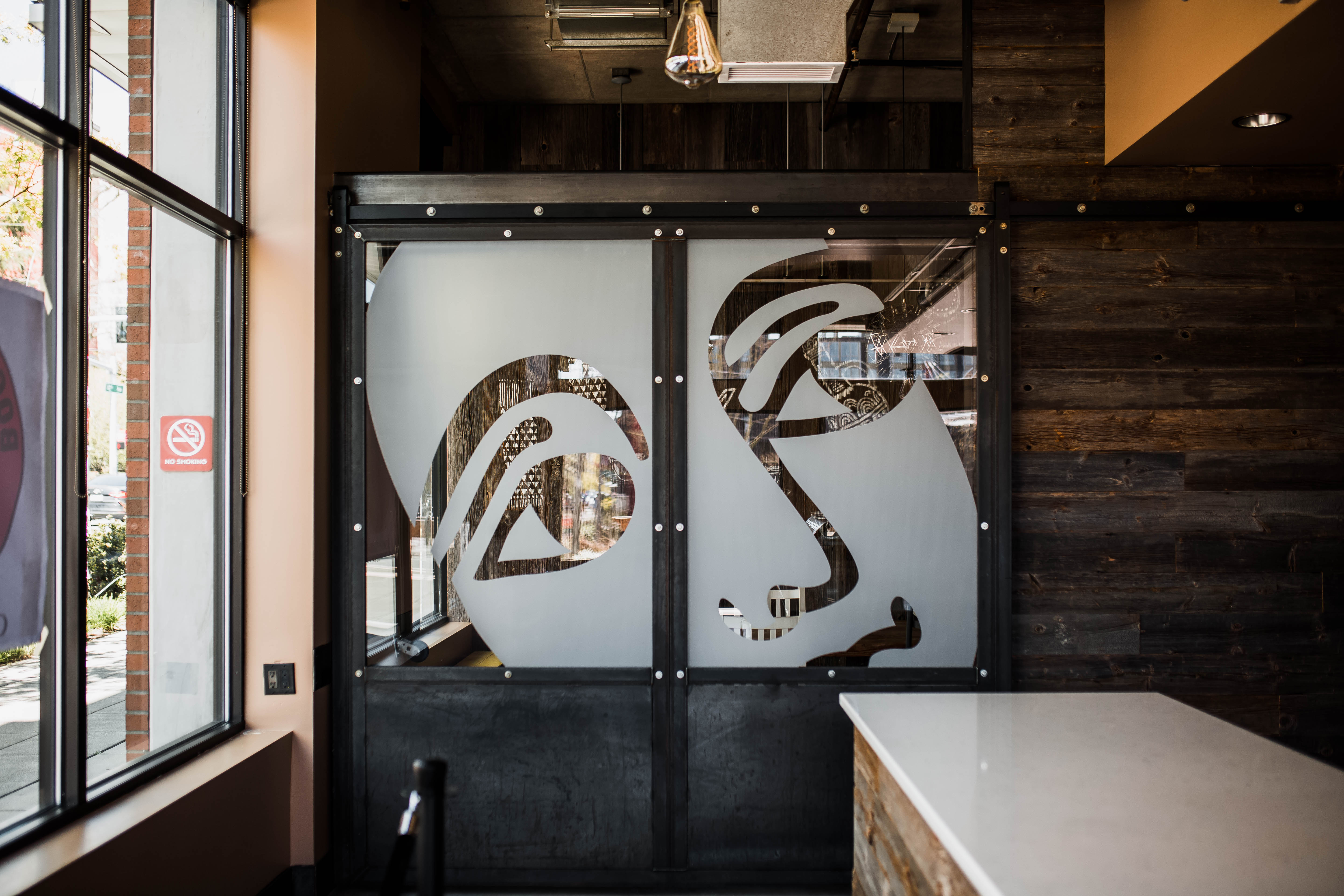 Two closed glass doors at Boon Boona coffee shop in Capitol Hill depict the company’s logo, a drawing of a human face looking off into the distance