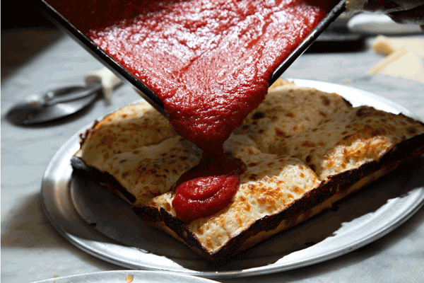 a gif of a detroit-style square pie with red sauce being poured over the top and cheese