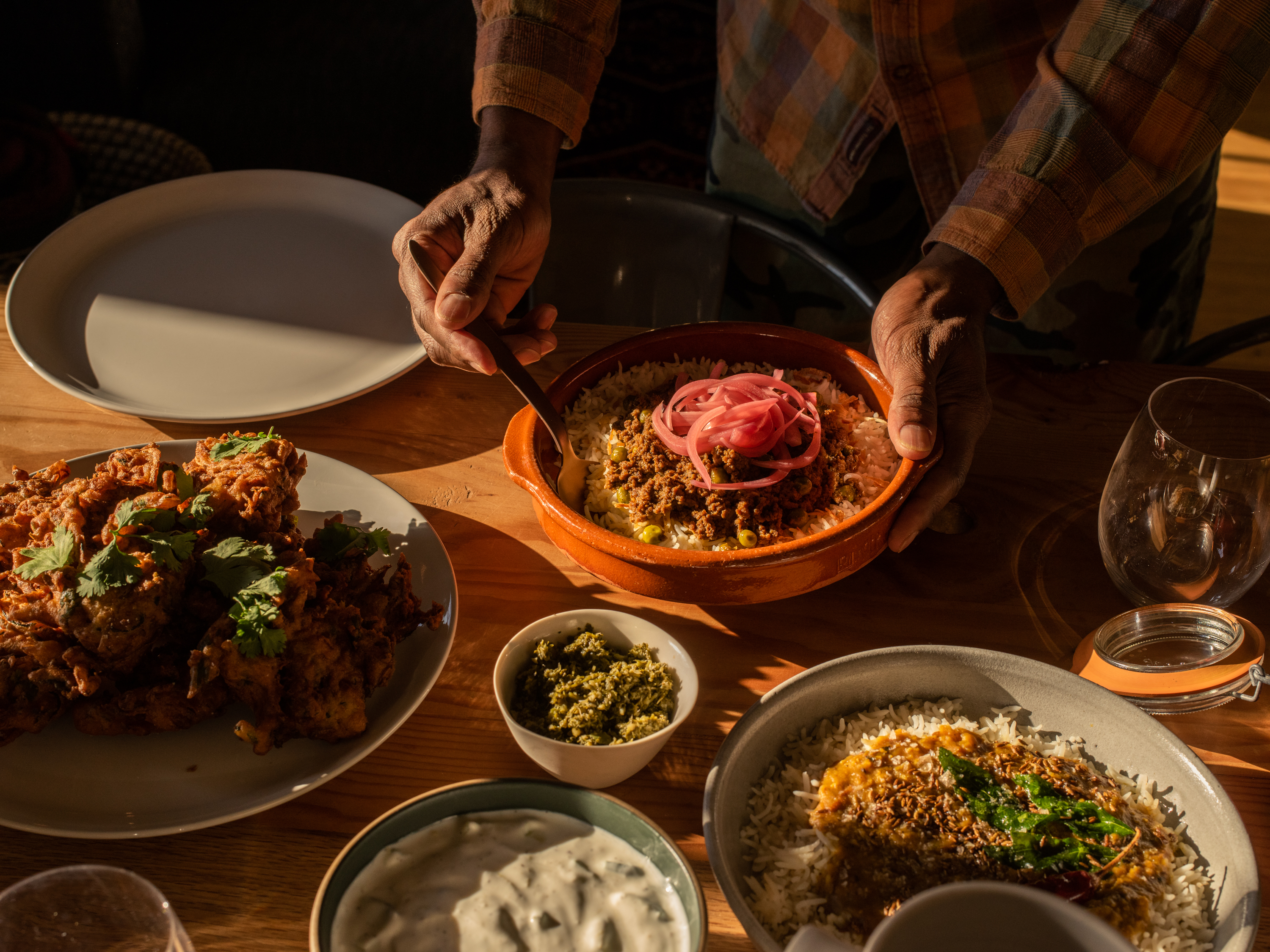 A selection of dishes from pop-up Karachi Cowboys on a table; one man in a flannel shirt presents a plate of kheema over rice with pickled onions on top