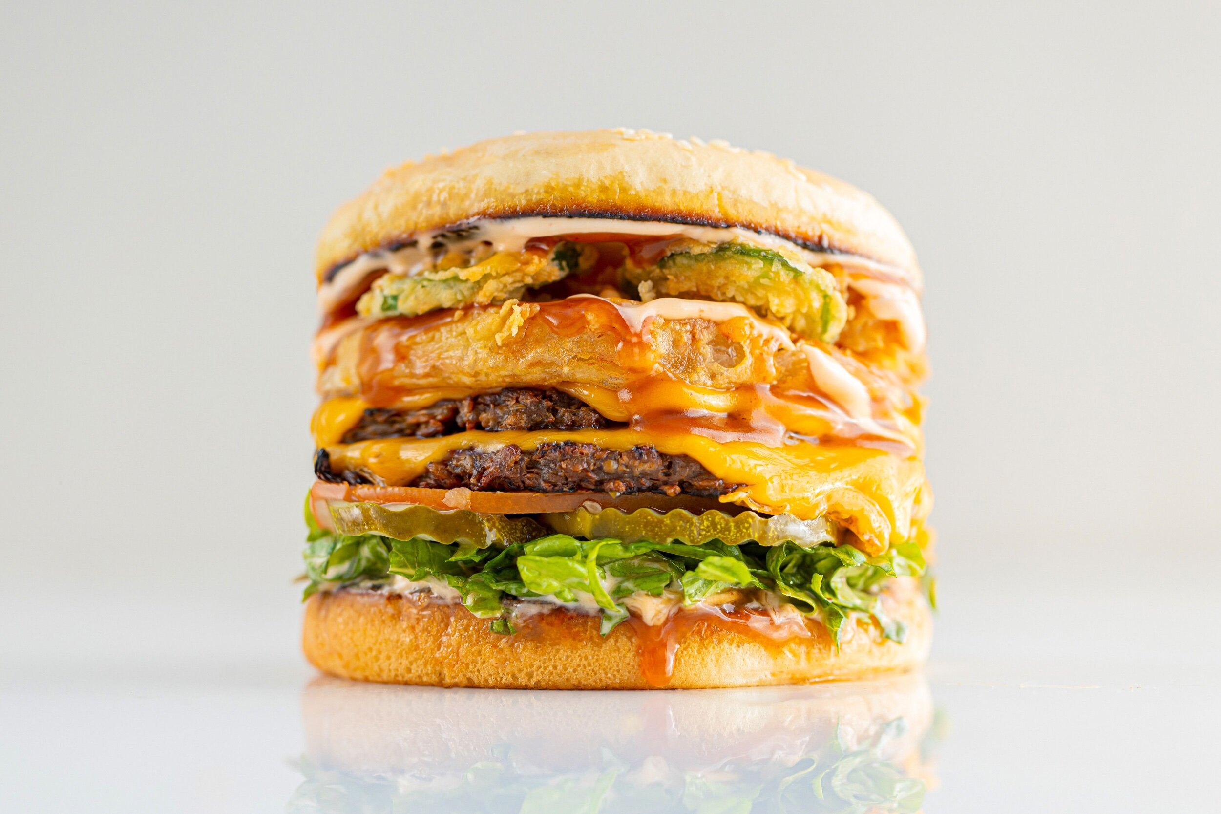 A stacked burger with fried ingredients and melty cheese on a white background.