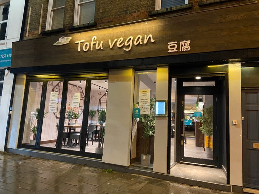The brown and glass exterior of Tofu Vegan restaurant on Upper Street, Islington, London, with tofu-coloured signage, blue Deliveroo signage in the windows
